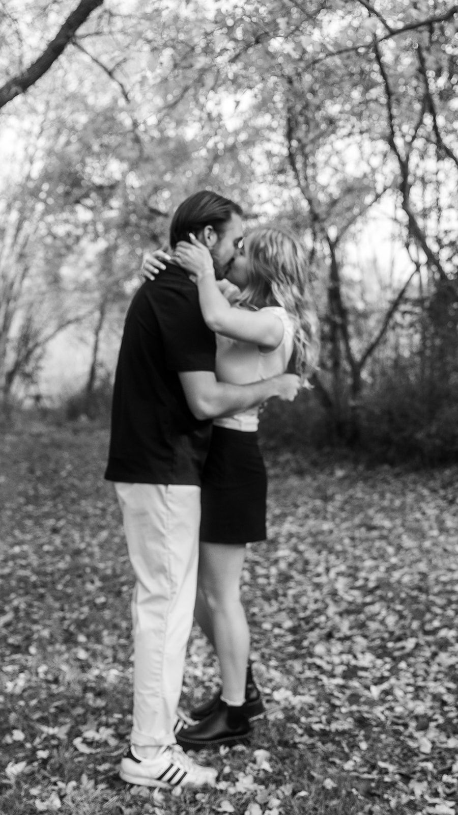 Black and white romantic sequence of couple embracing in leaf-covered woods.
