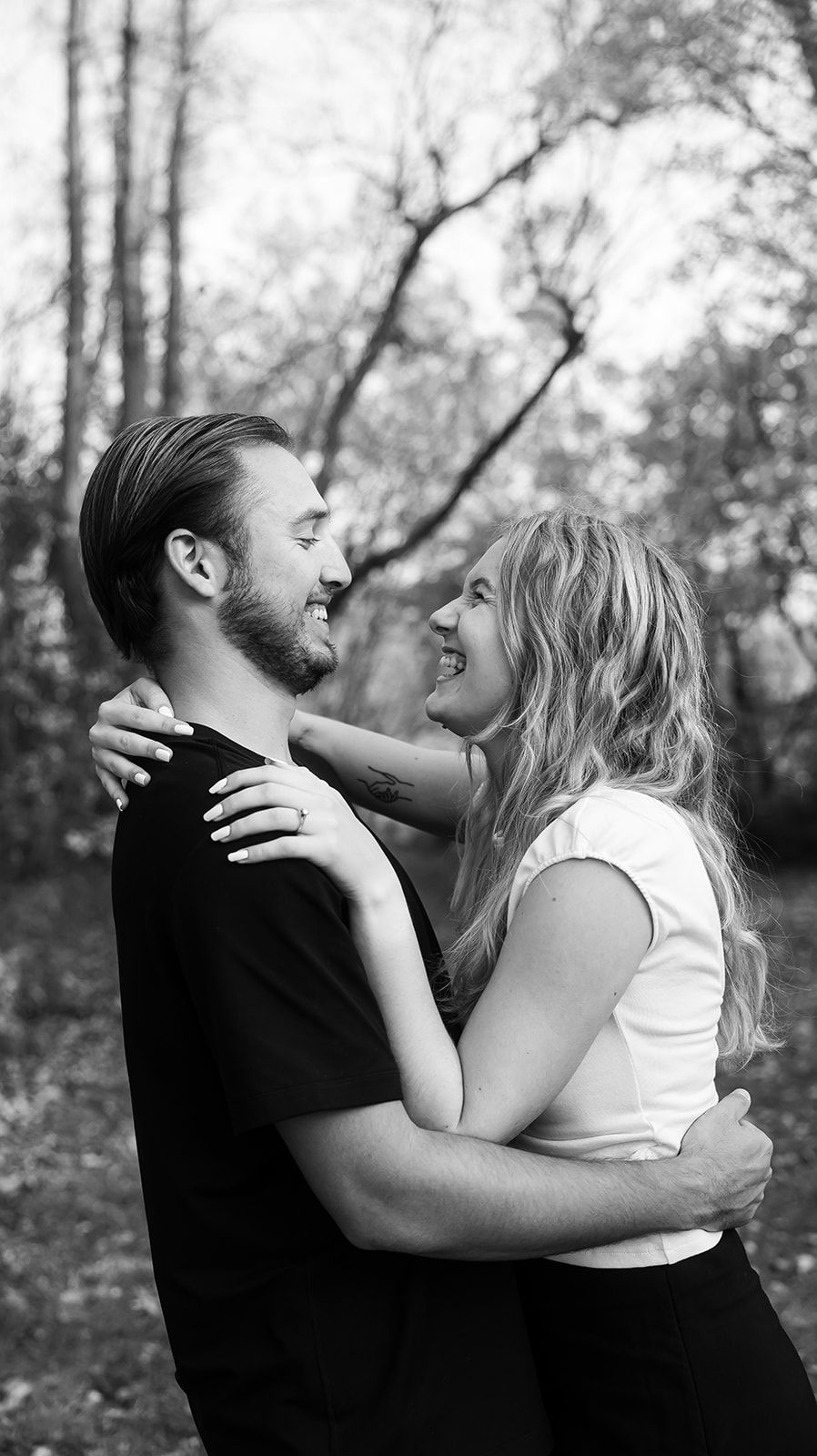 Black and white photo of a couple embracing intimately outdoors.