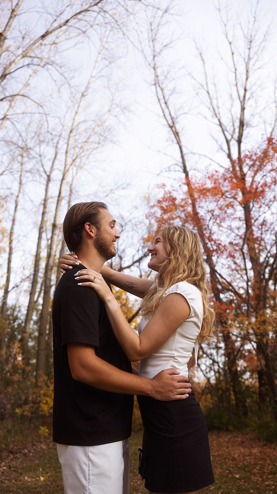Playful couple in contrasting outfits pose against bare winter trees.
