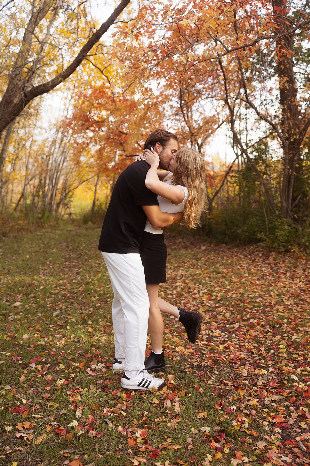 Dancing couple embraces in a scenic fall setting with orange and yellow foliage.