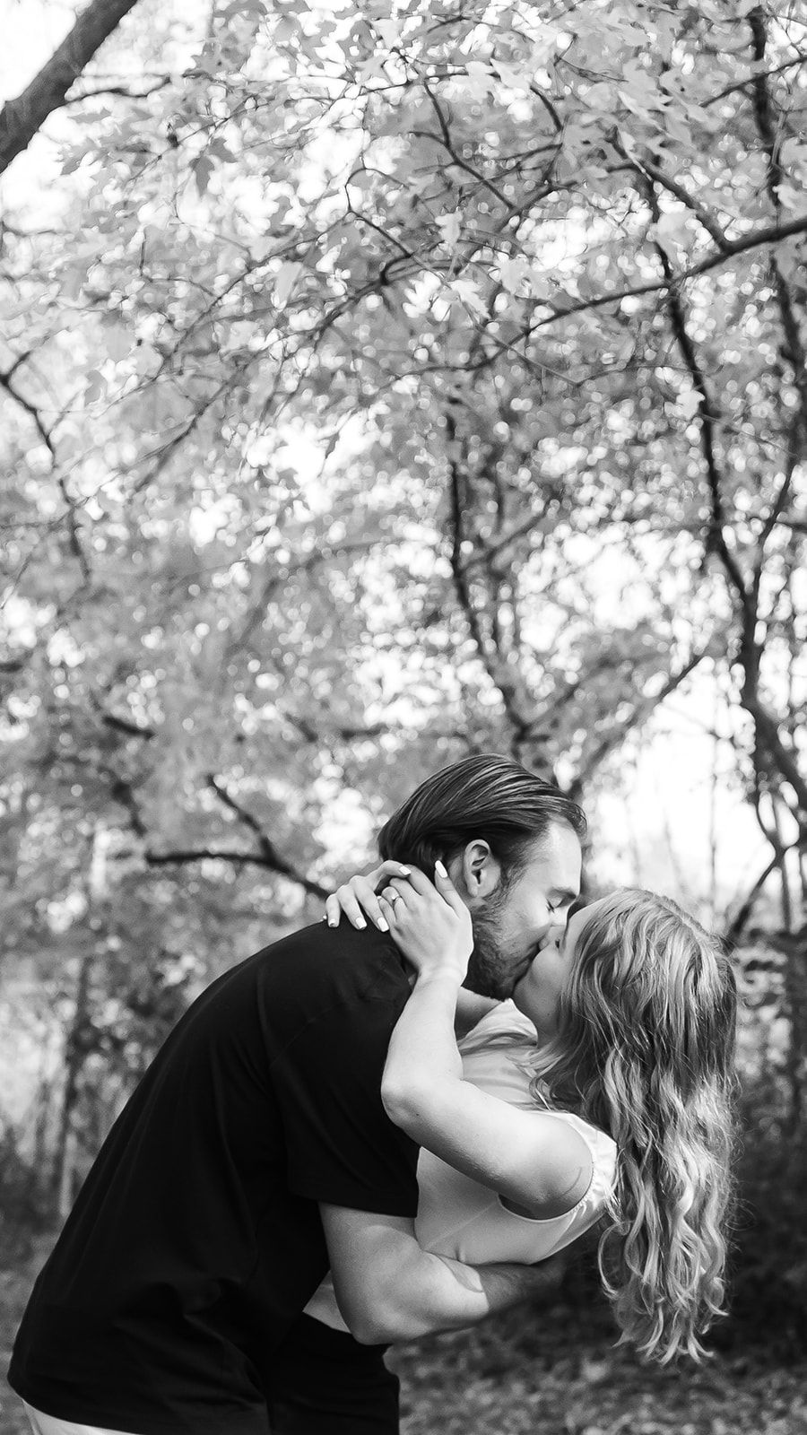 Black and white romantic portrait with a dramatic dip pose under blooming trees.