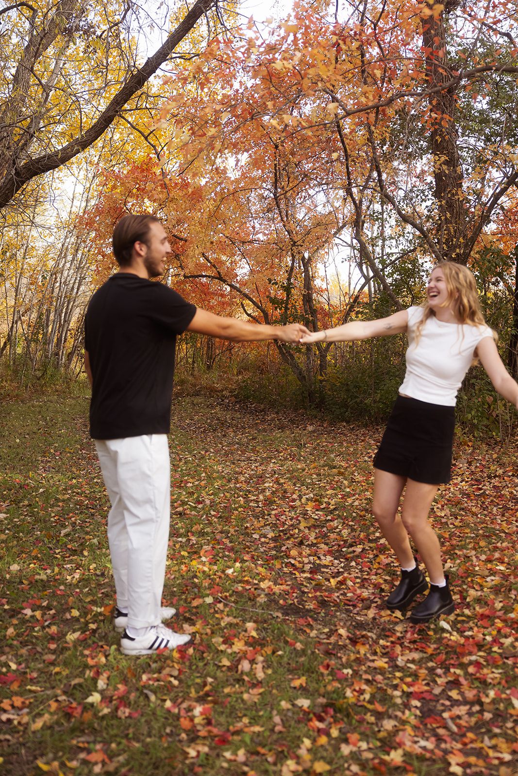A romantic autumn photo shoot in a wooded area with fallen leaves and golden trees.