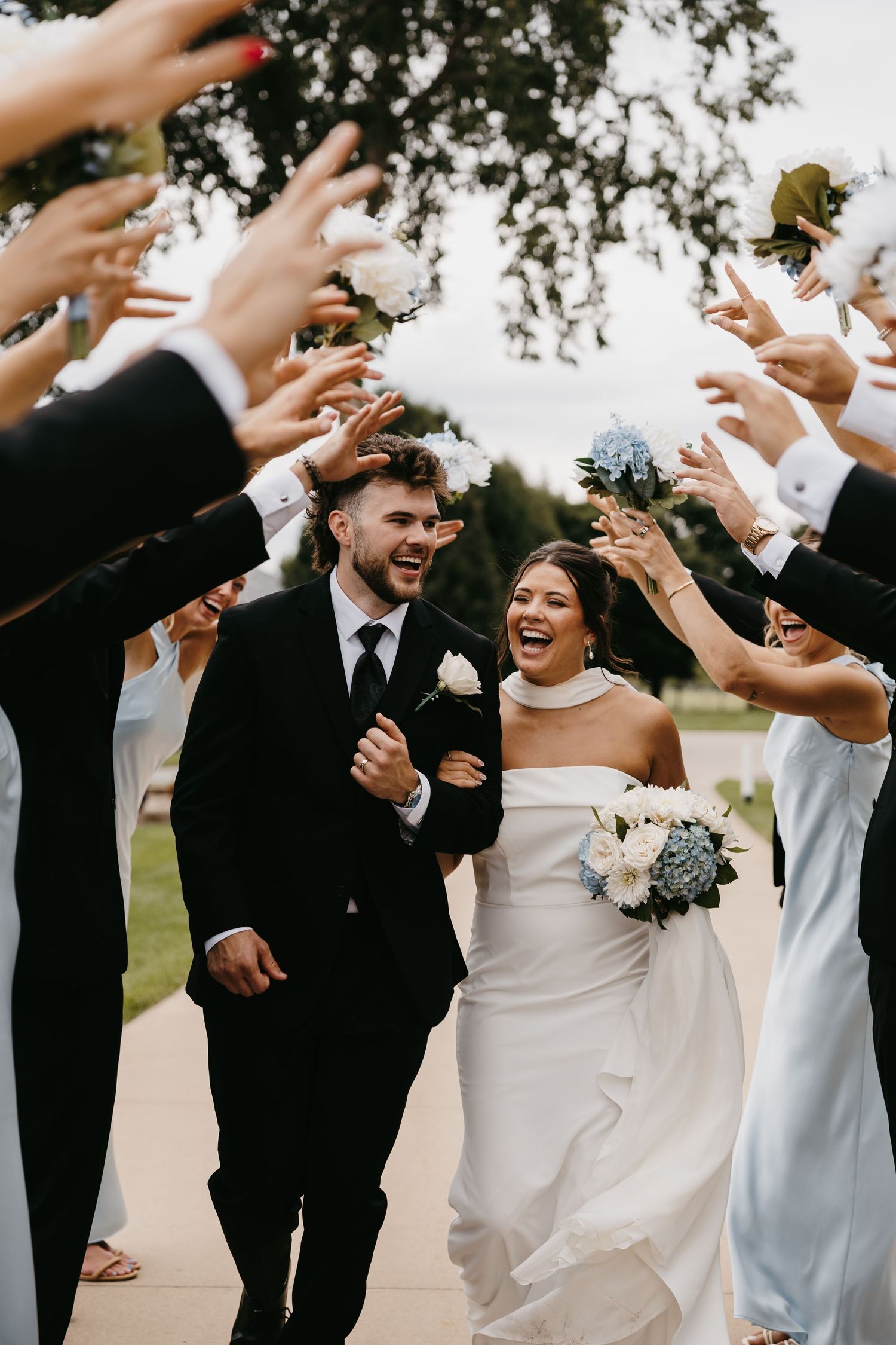 Wedding party celebrates joyfully walking together outdoors in formal attire.