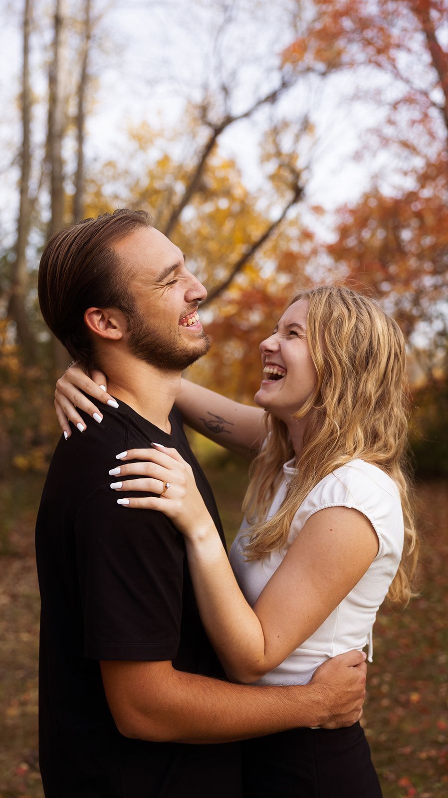Intimate portrait of couple laughing together in autumn woodland setting.