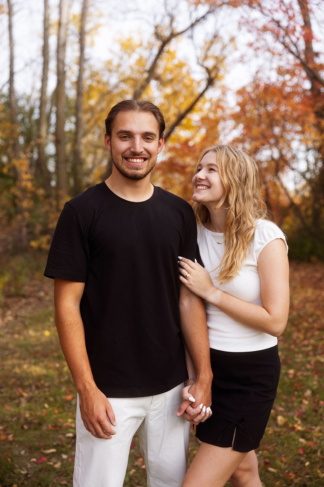 A couple shares genuine smiles while posing in a fall forest setting.