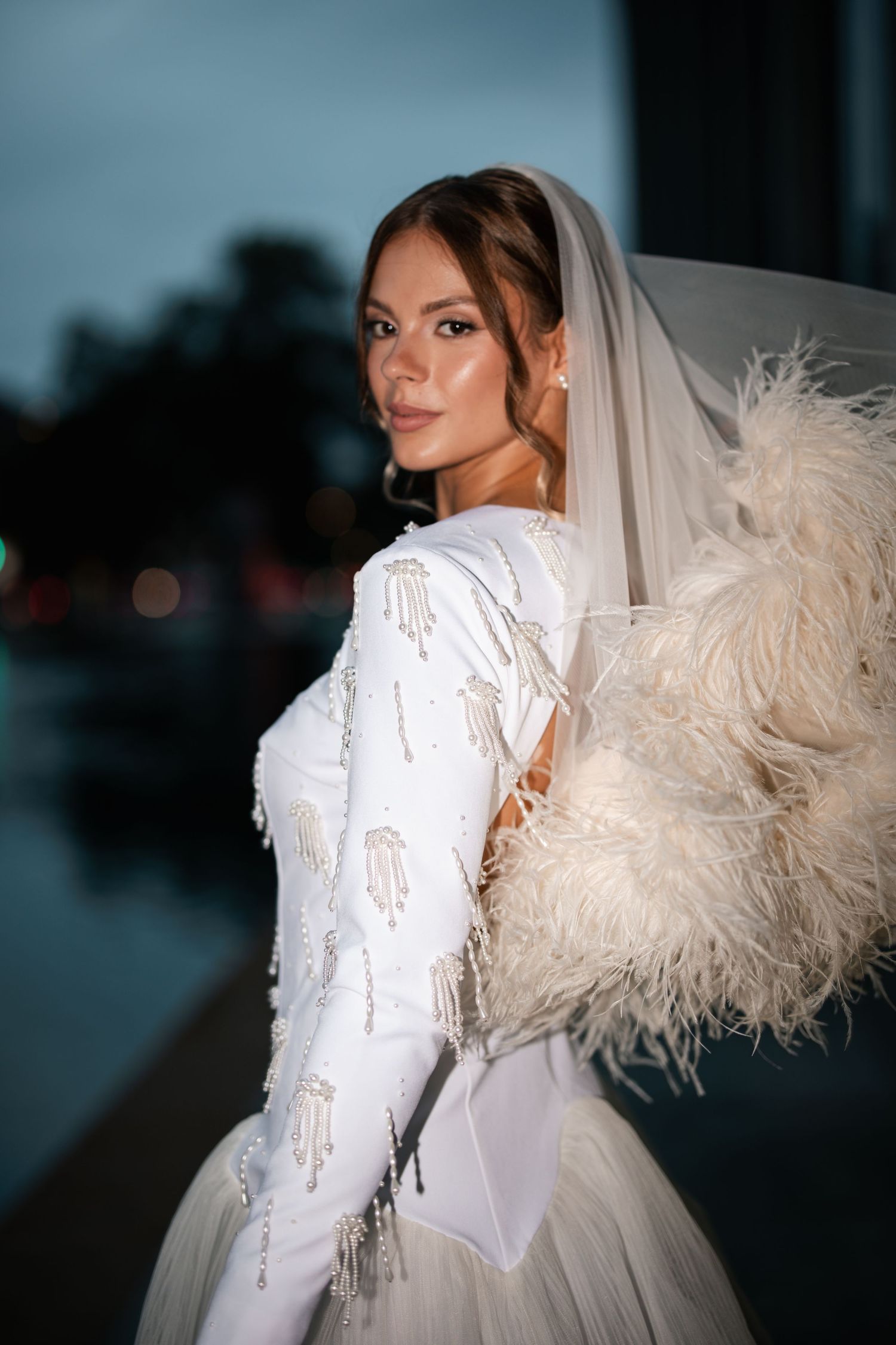 White wedding gown with feather details and delicate embellishments in dramatic lighting.