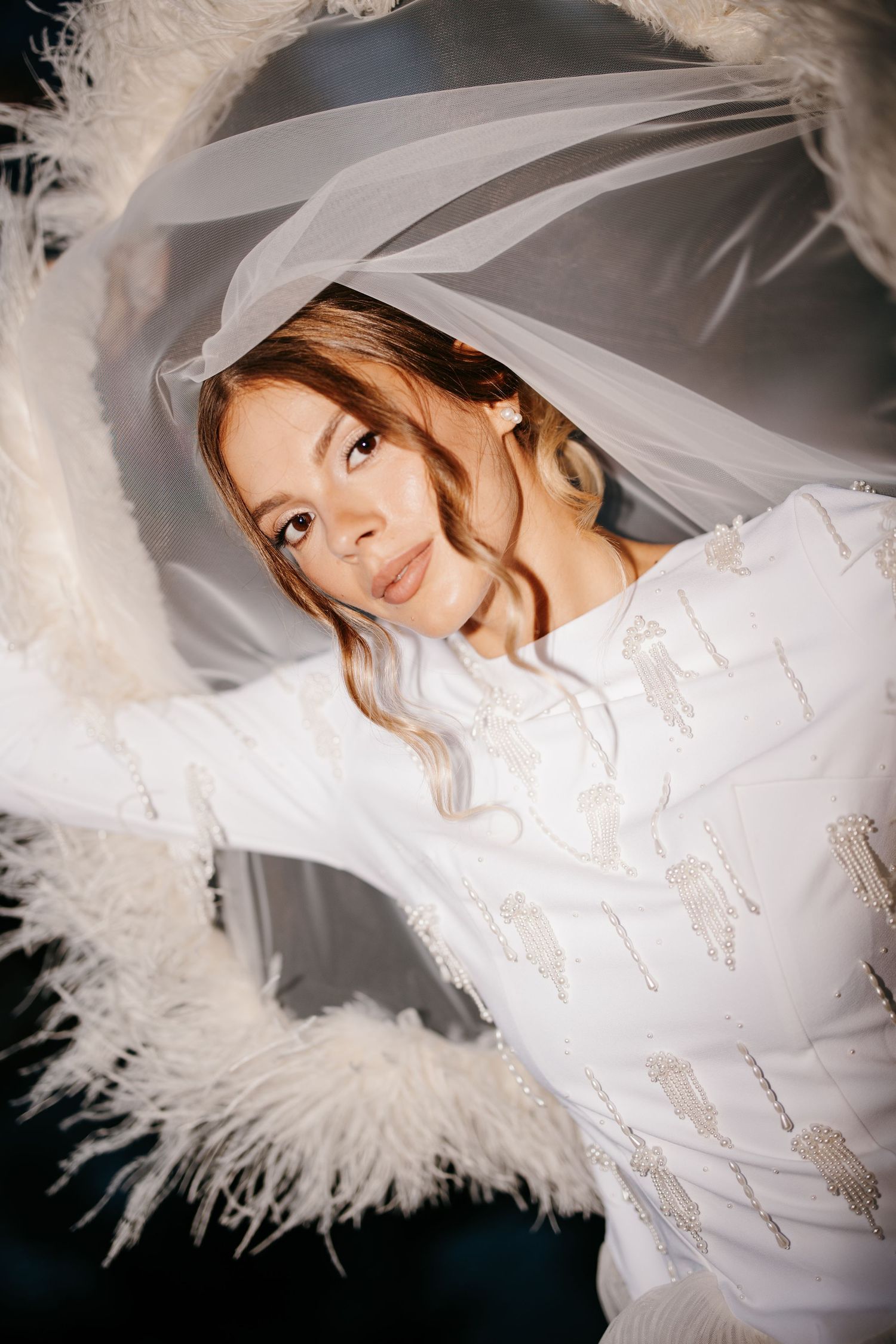 Artistic bridal portrait featuring a white gown with feather accents and veil.
