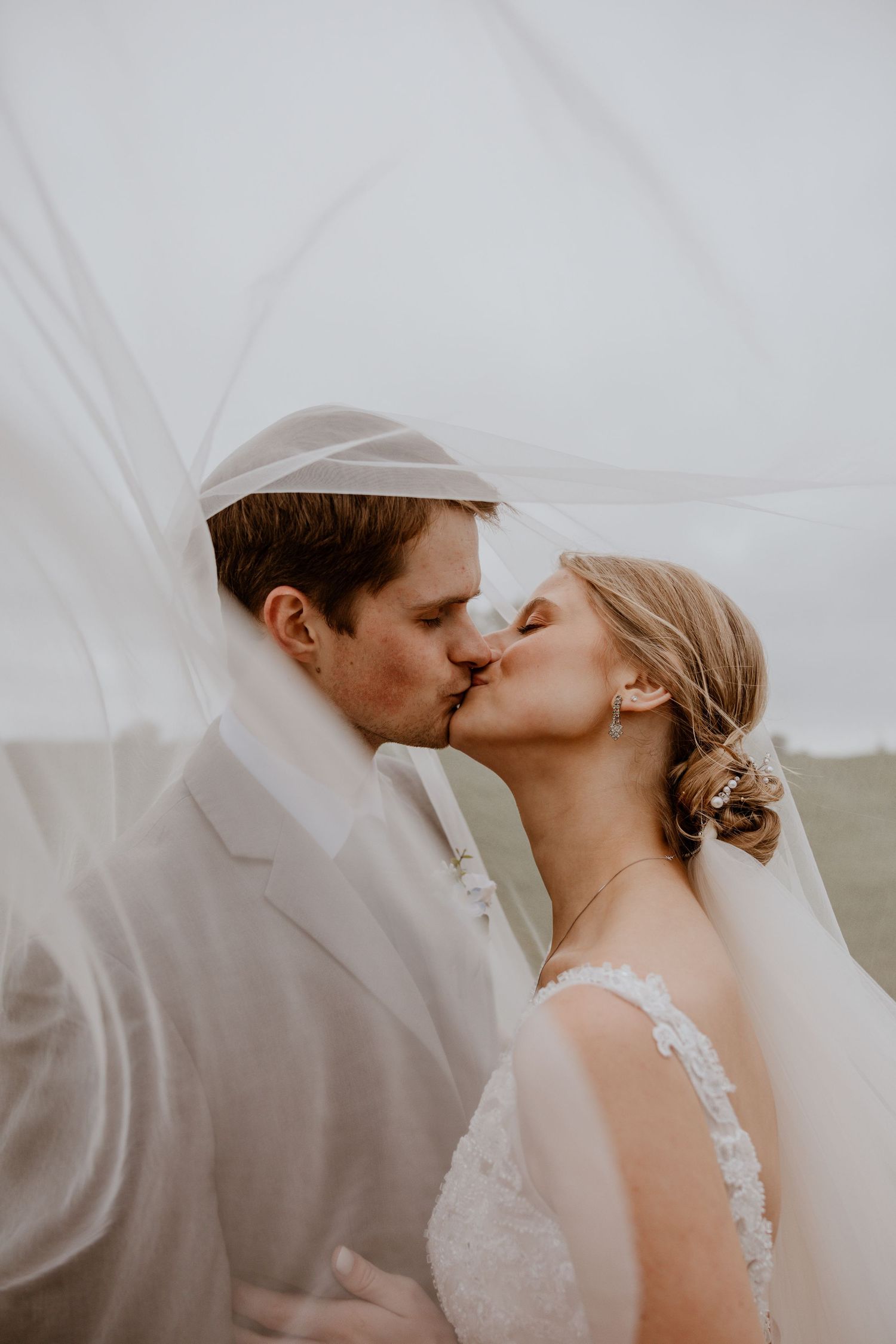 Romantic wedding moment captured through flowing white veil in soft light.