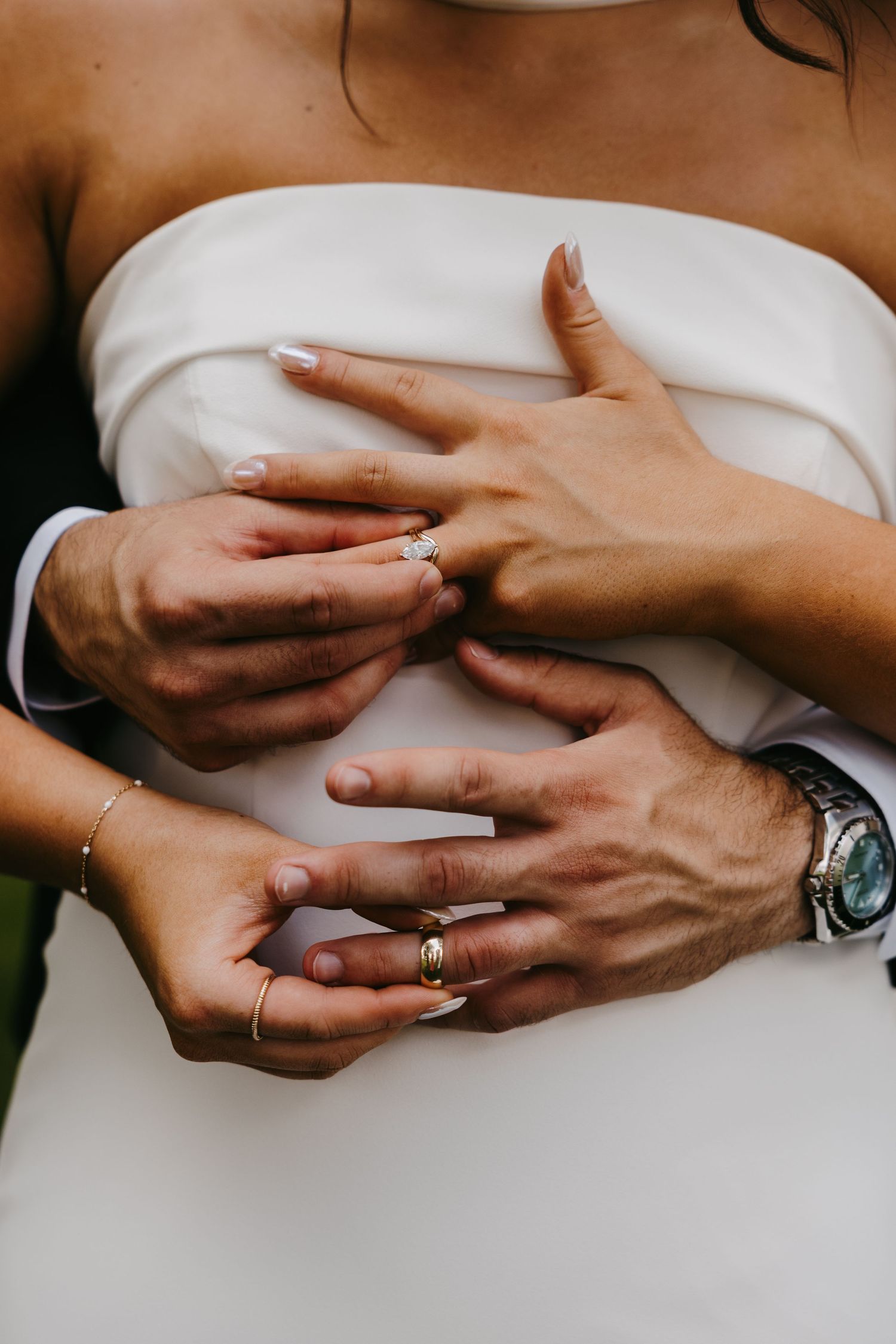 Close-up of hands with wedding rings against white dress fabric.