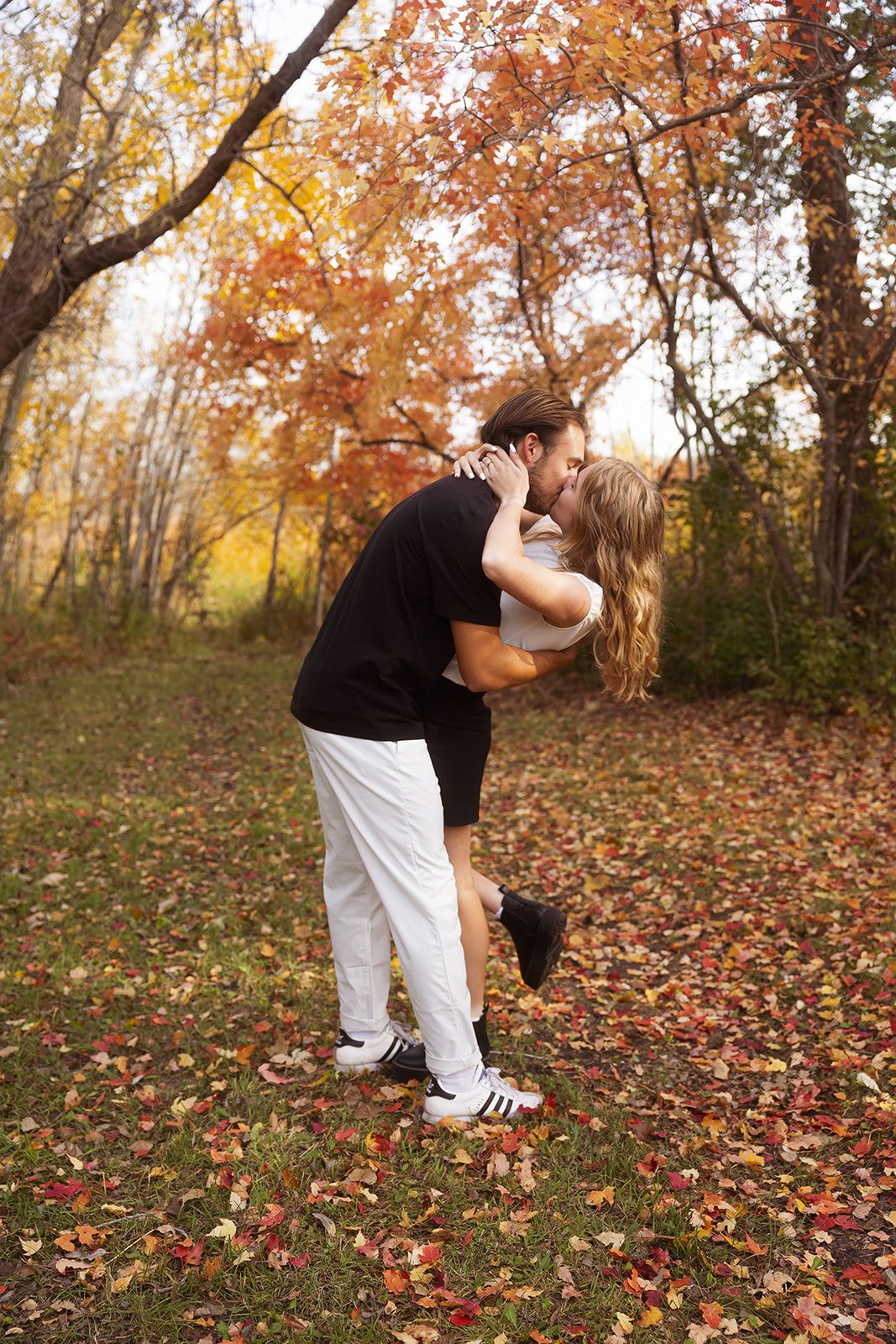 Romantic dip pose captured during an autumn photoshoot with colorful leaves on the ground.