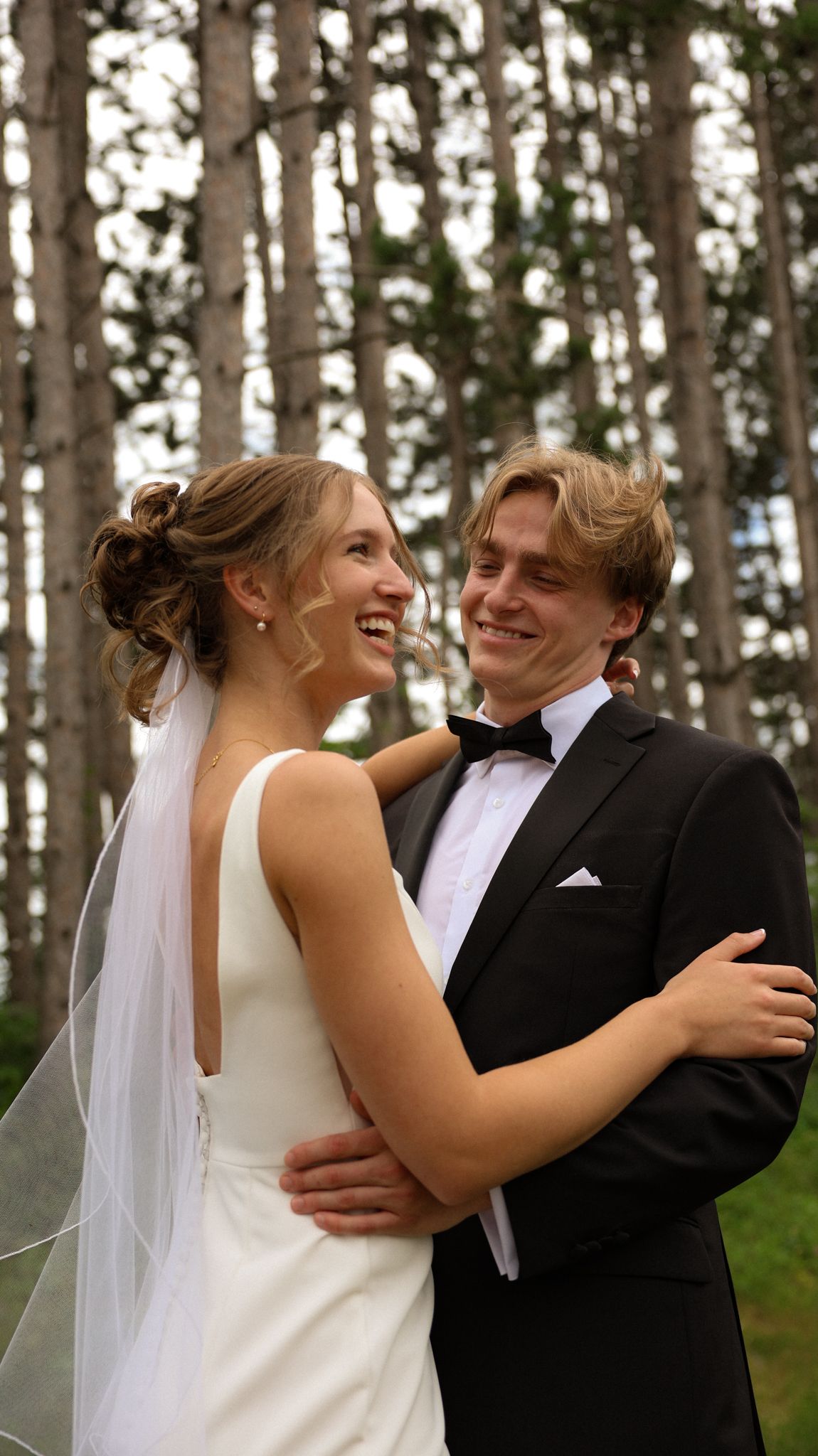 Joyful wedding couple sharing candid moments among pine trees.