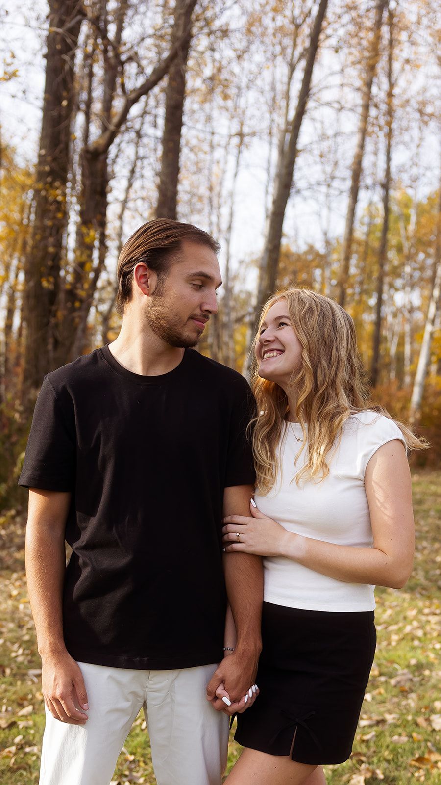 A couple shares genuine laughter while posing in a wooded autumn setting.