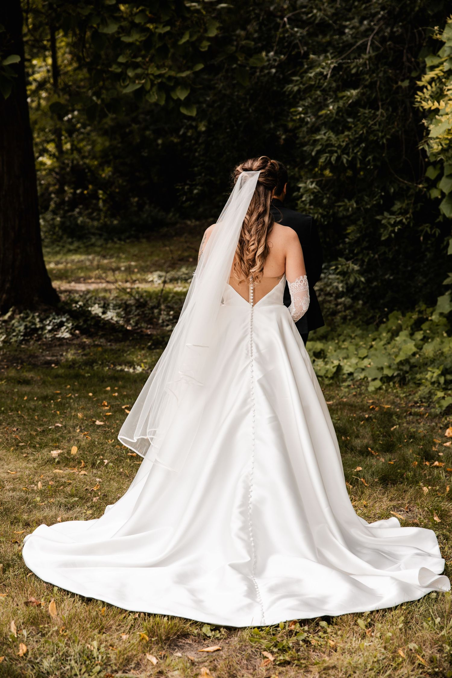 Back view of a classic white wedding gown with flowing train in a forest setting.