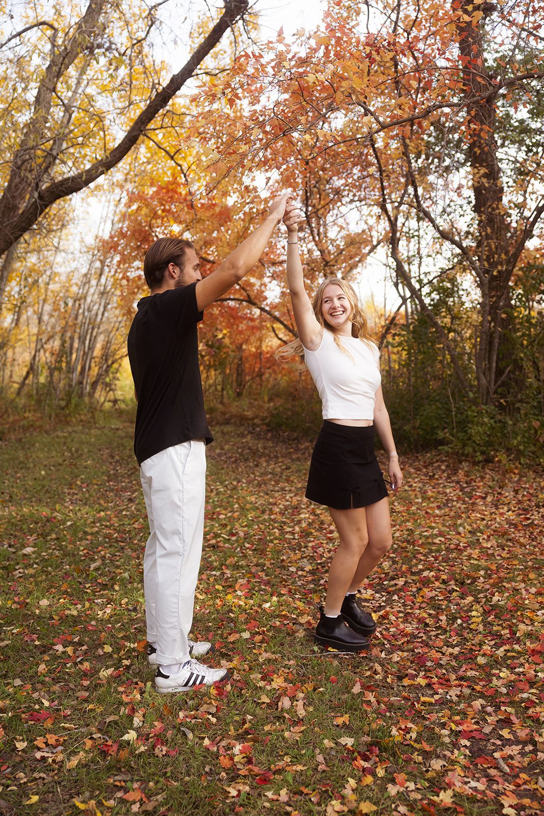 Couple performing dance lift moves in autumn forest with fallen leaves.