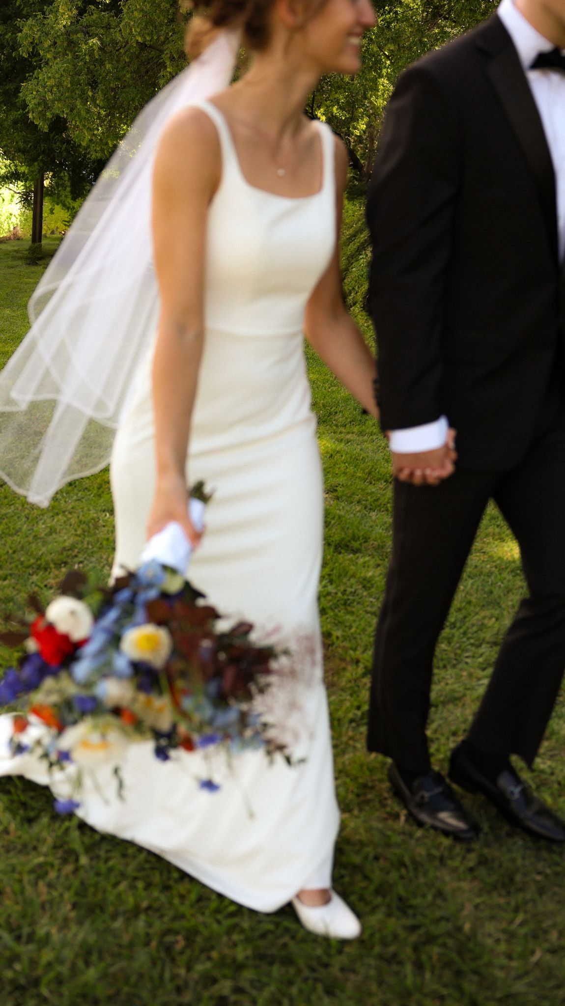 Close-up view of a bride's white dress and colorful bouquet against green grass.