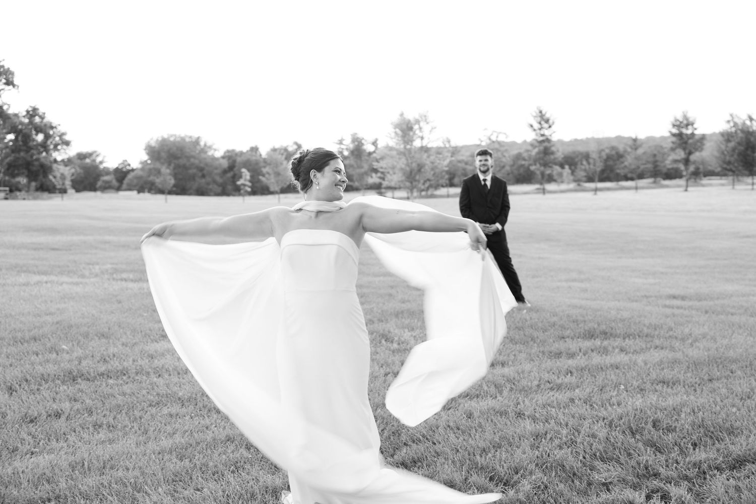 Black and white wedding photo with flowing veil in an open field.