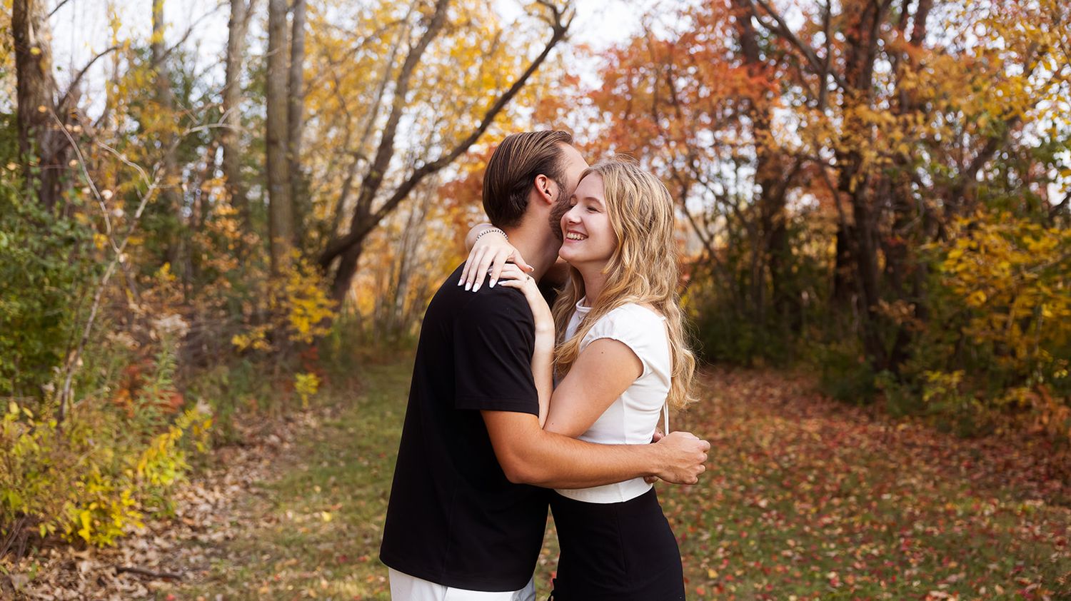 Panoramic autumn forest scene with couple in intimate embrace.