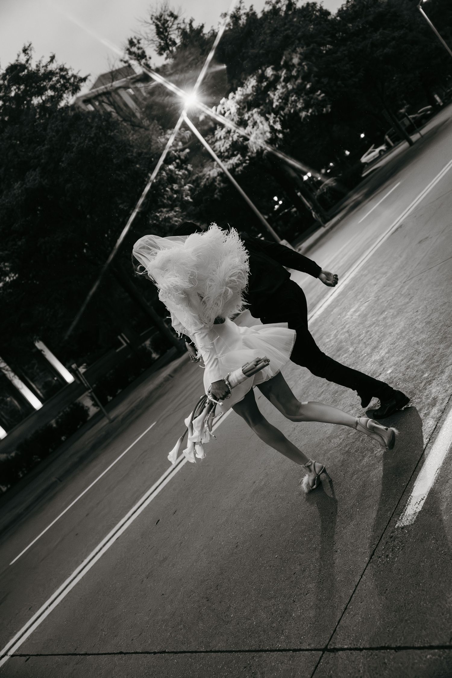 Black and white photo of newlyweds dancing on an empty street at dusk.