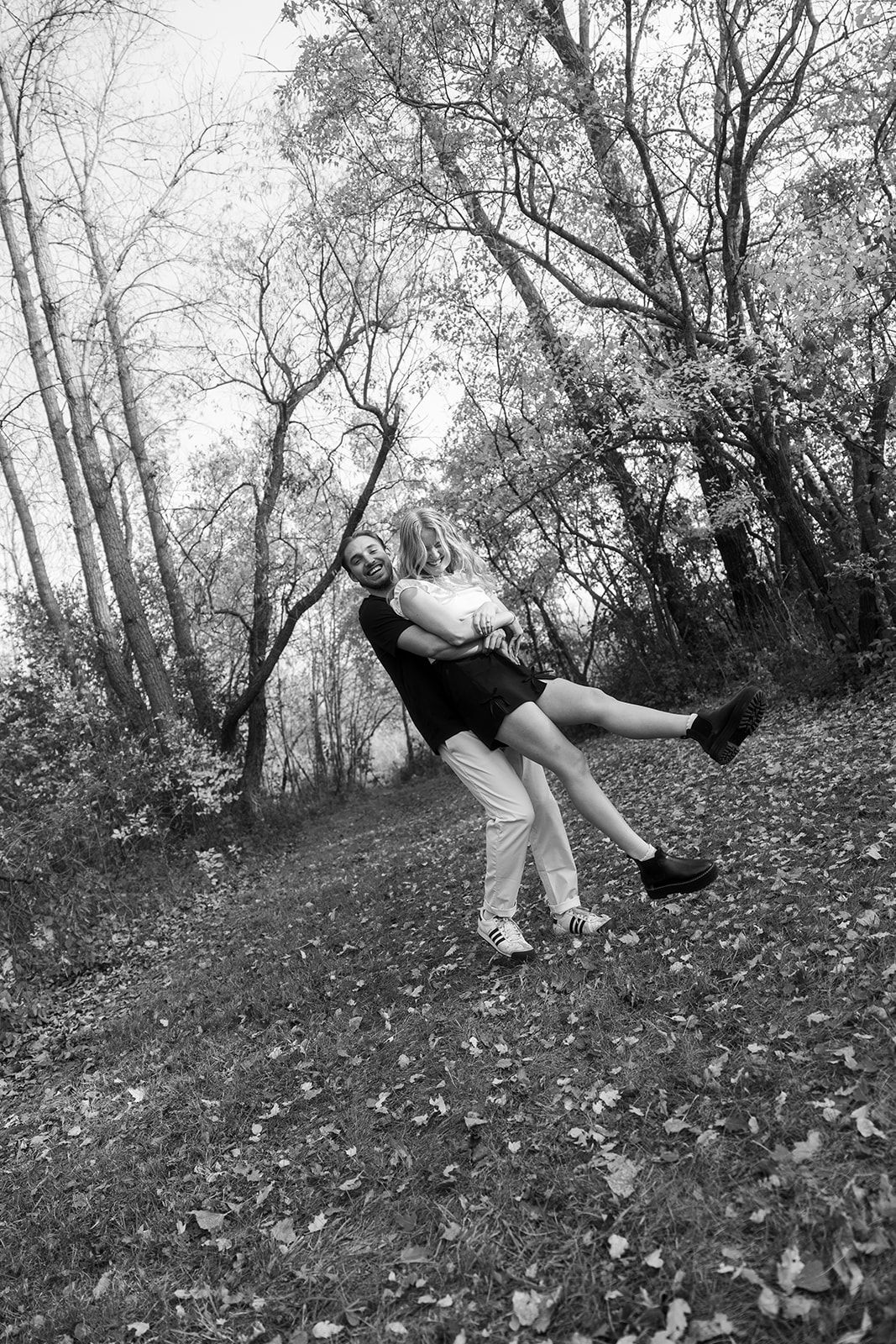 Black and white photo of couple doing a romantic dip pose among fallen leaves.