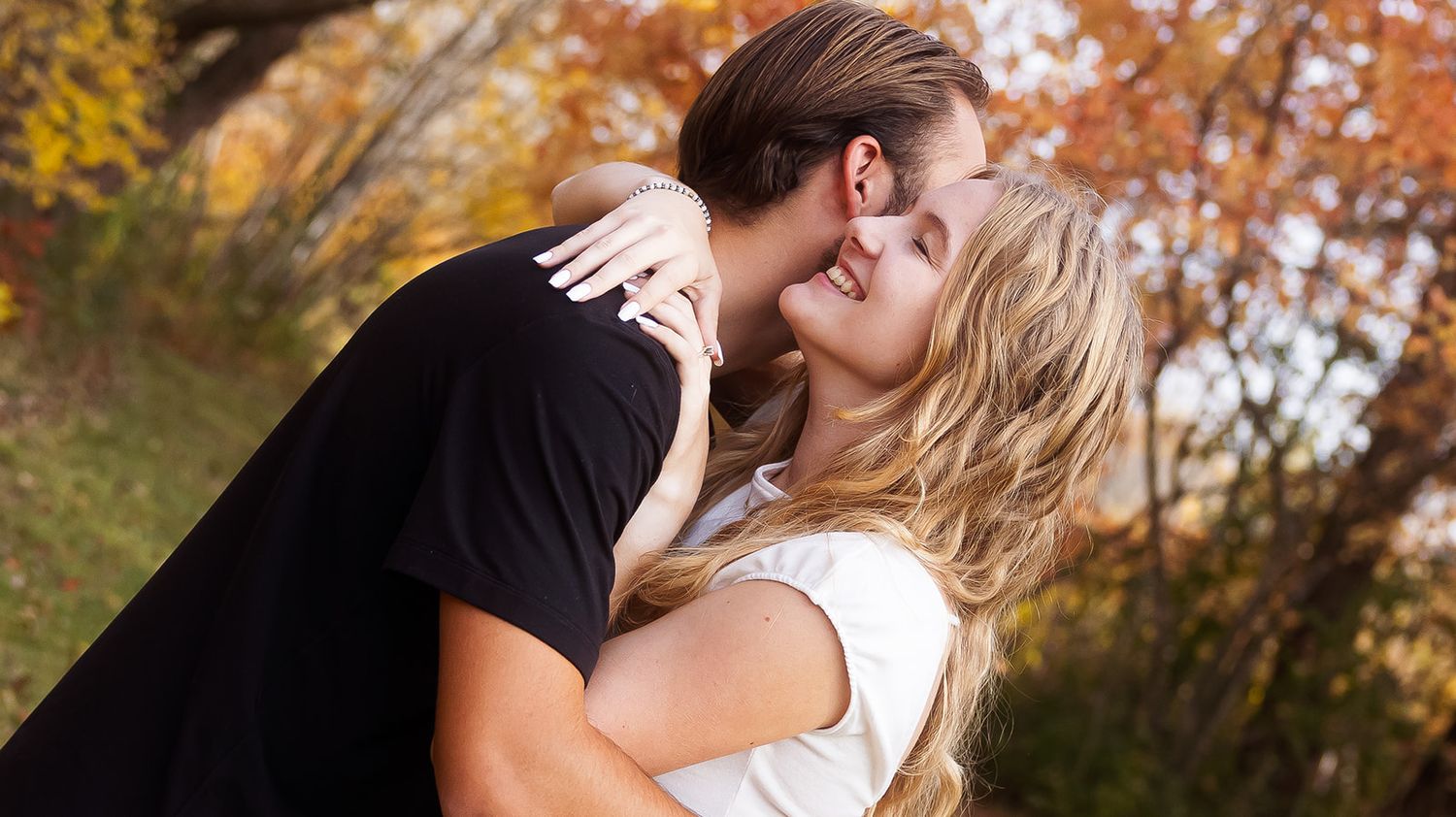 Close-up shot of couple sharing tender moment with fall foliage in background.