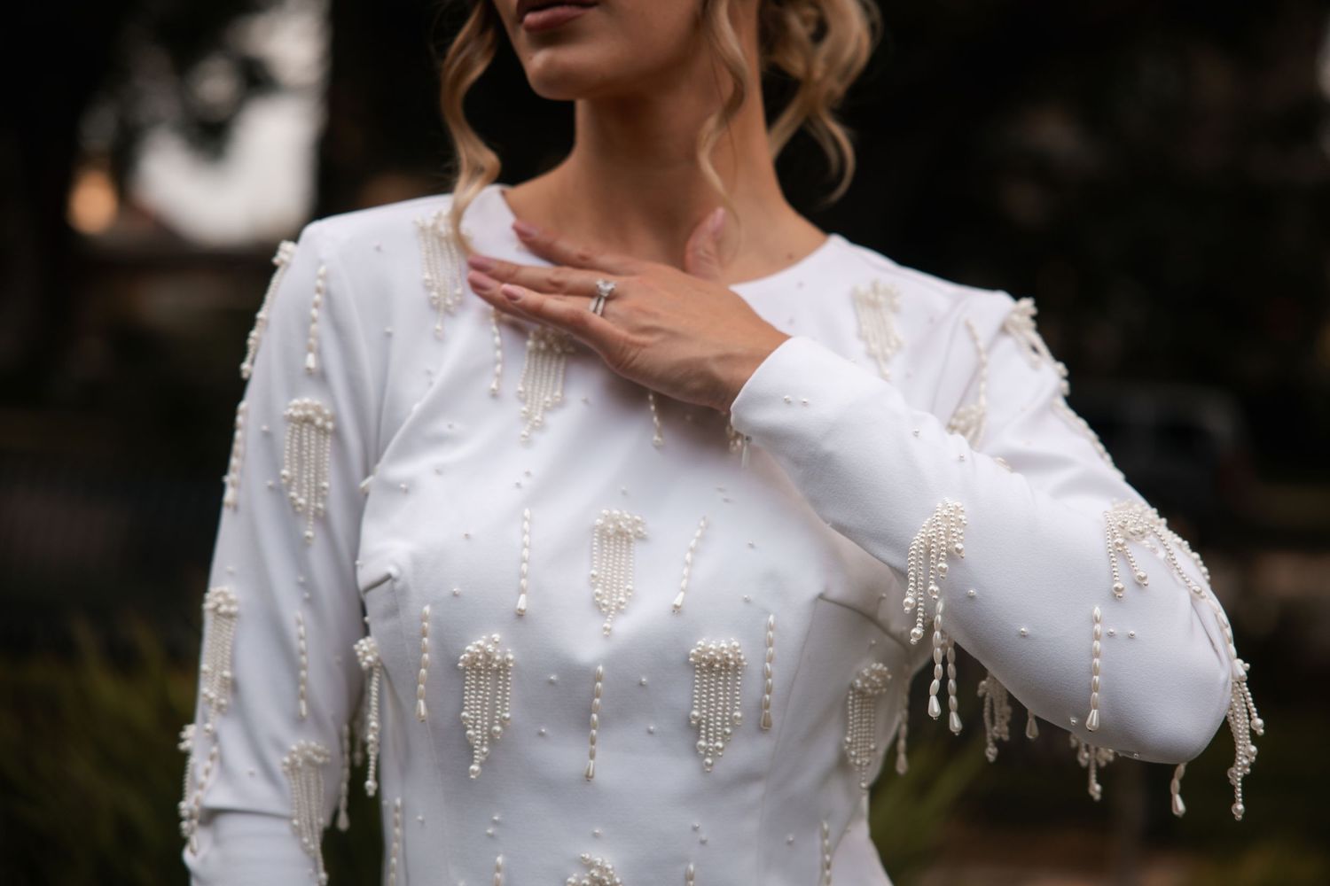 Close-up detail of an elegant white wedding dress with delicate beaded embellishments and long sleeves.