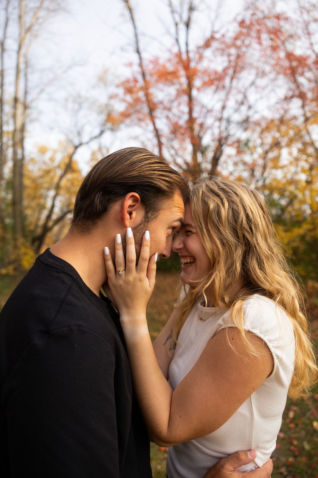 A couple in black and white clothing share an intimate embrace among autumn trees.