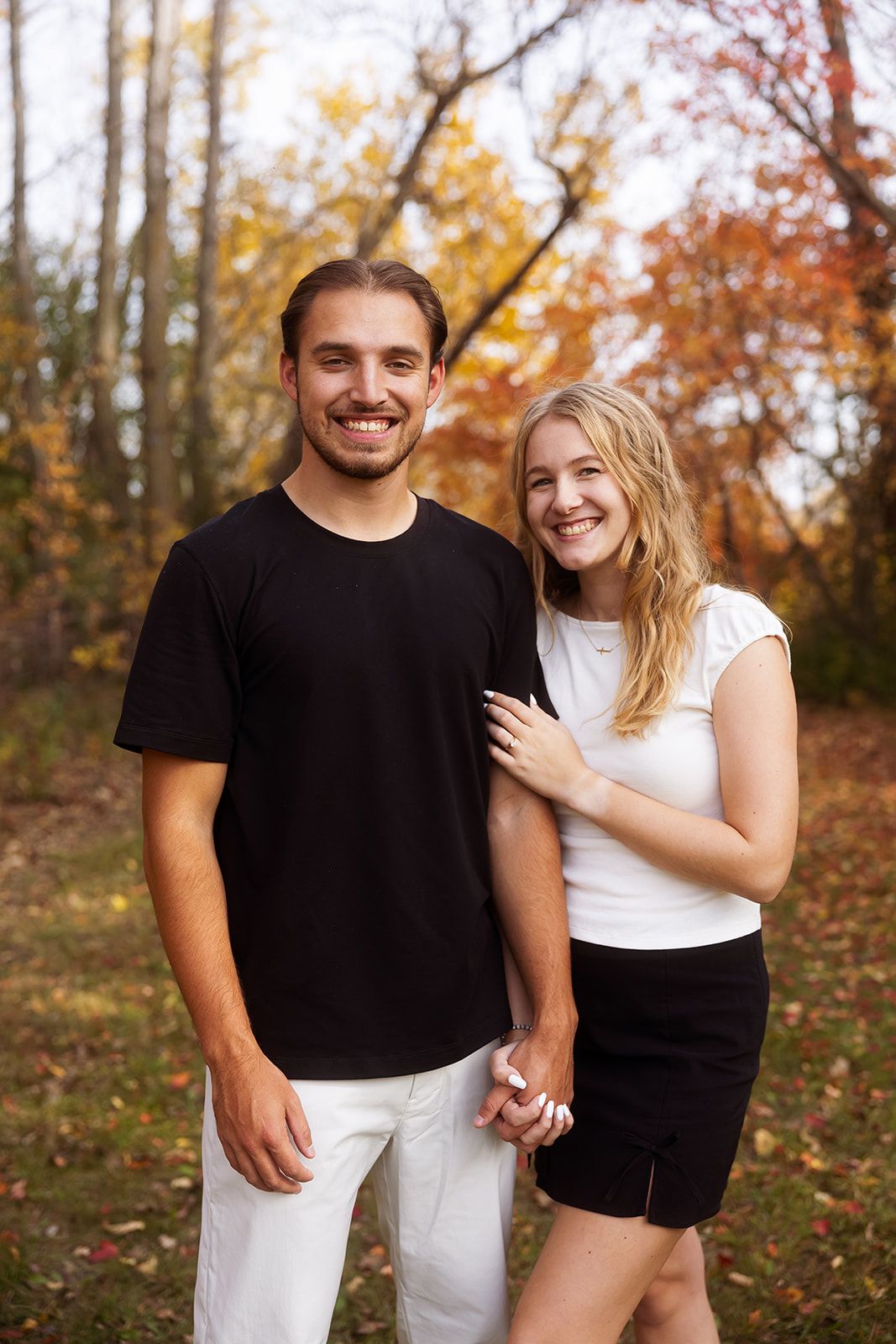 A couple in black and white outfits share playful moments in a fall forest setting.