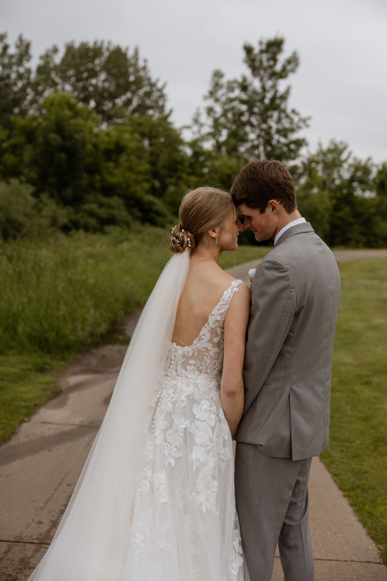 Newlyweds share tender moments on a path surrounded by greenery.