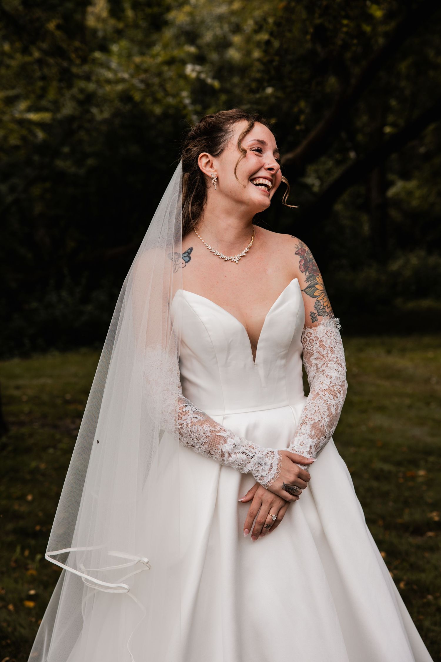 Bride in an elegant white dress with lace sleeves smiles during outdoor wedding photography.