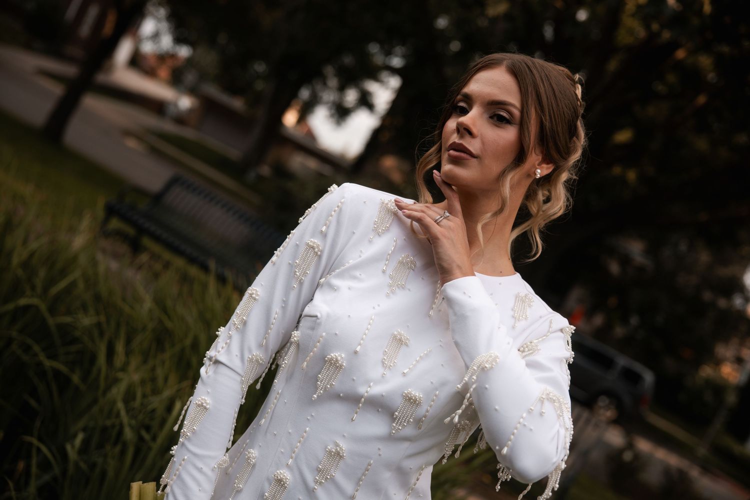 A close-up portrait of a woman in an elegant white long-sleeved dress outdoors.