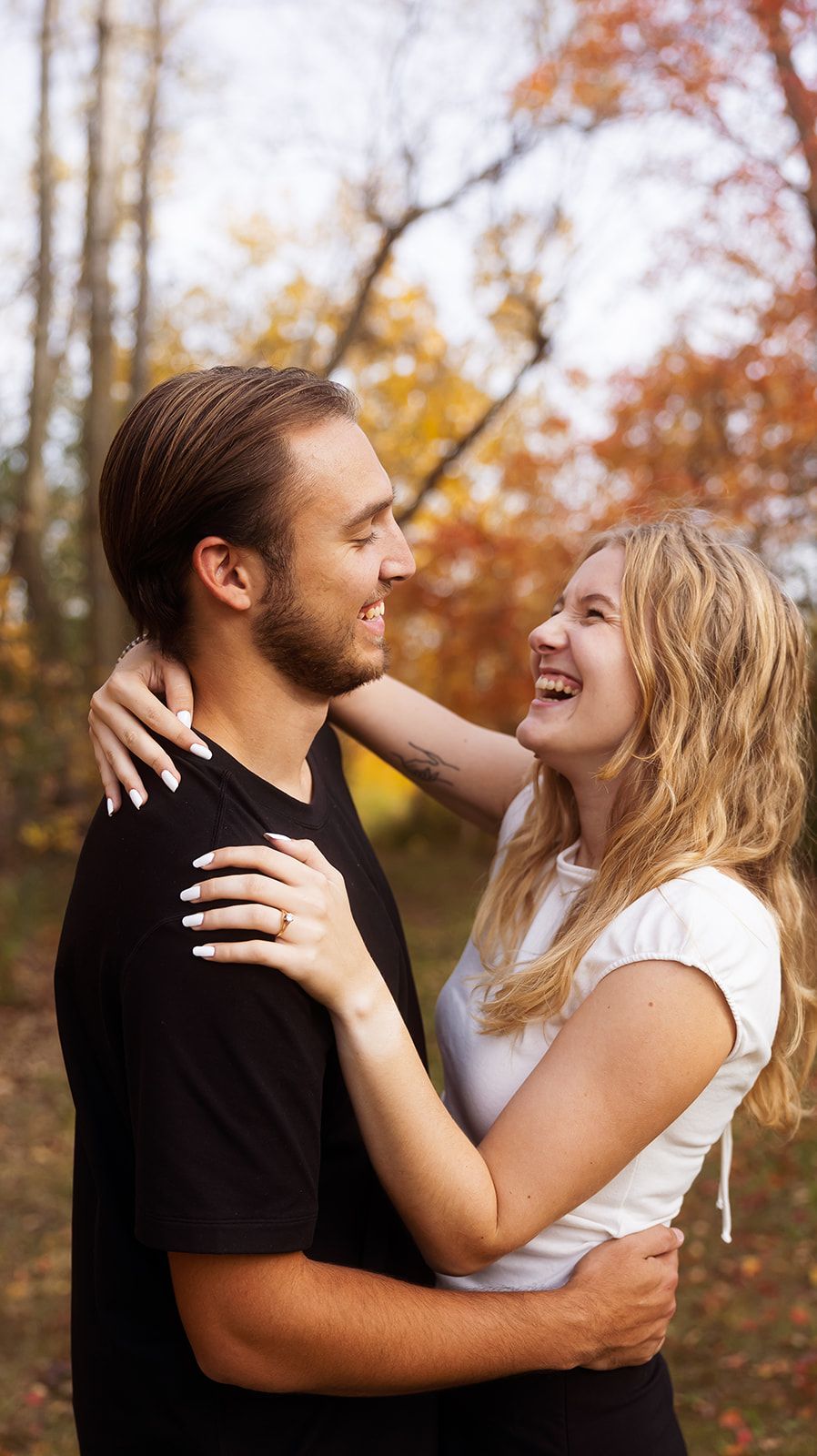 Couple embraces while sharing joyful moment in fall forest.
