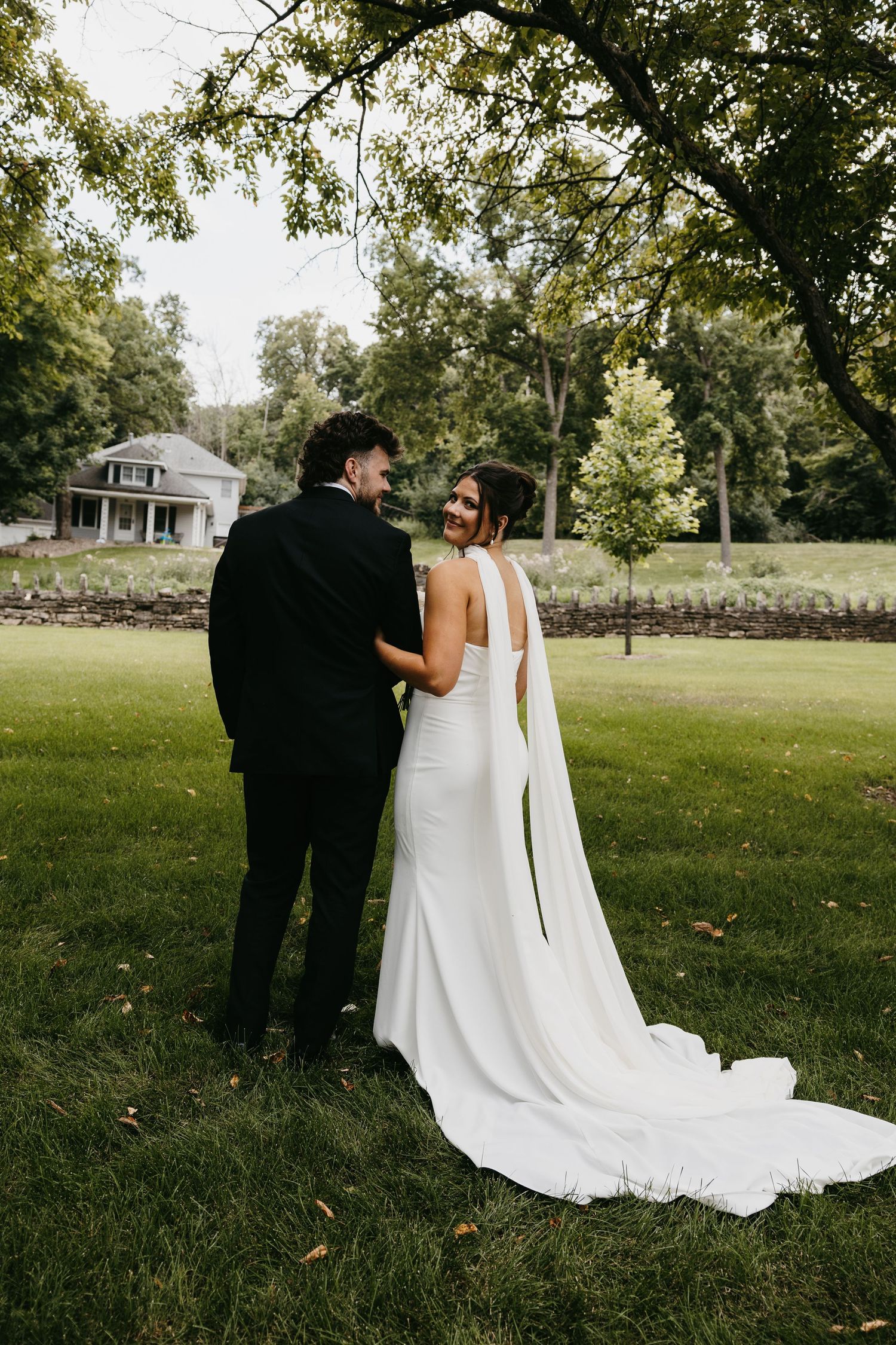 Elegant wedding couple photographed from behind in outdoor garden setting with flowing white dress.