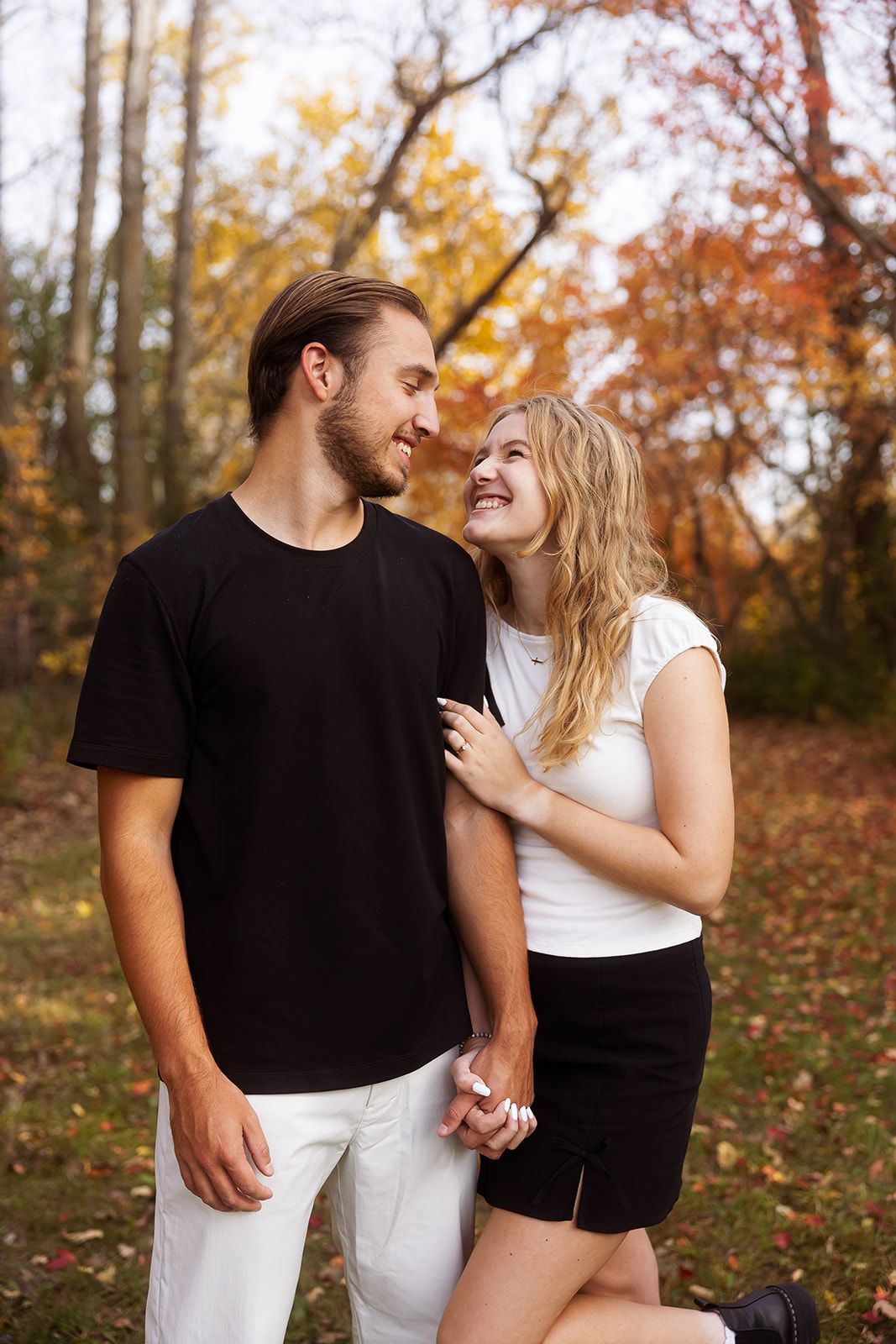 Romantic couple laughs together against autumn foliage backdrop.