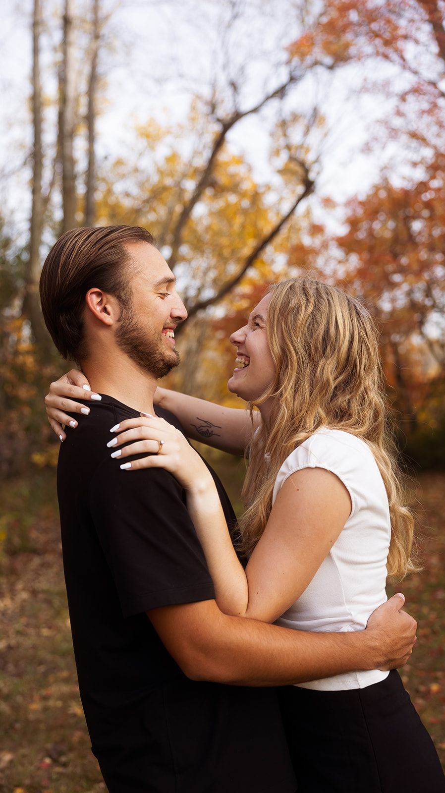 Couple shares tender moment among fall trees with golden leaves.