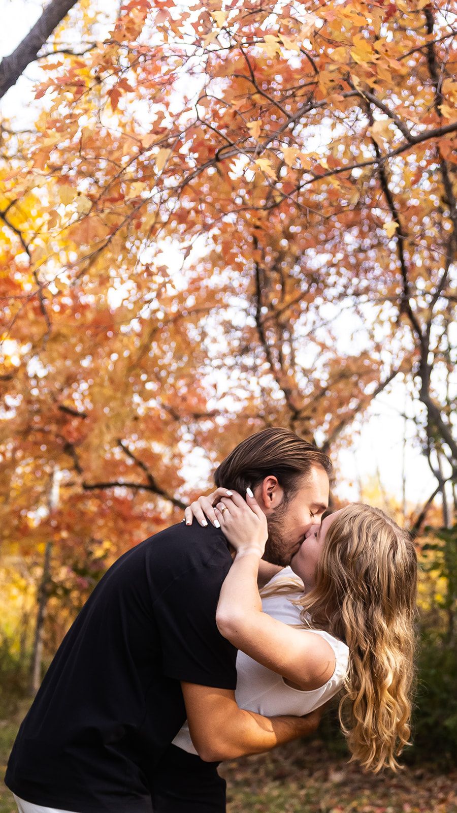Couple sharing an intimate moment under vibrant autumn trees with golden leaves.