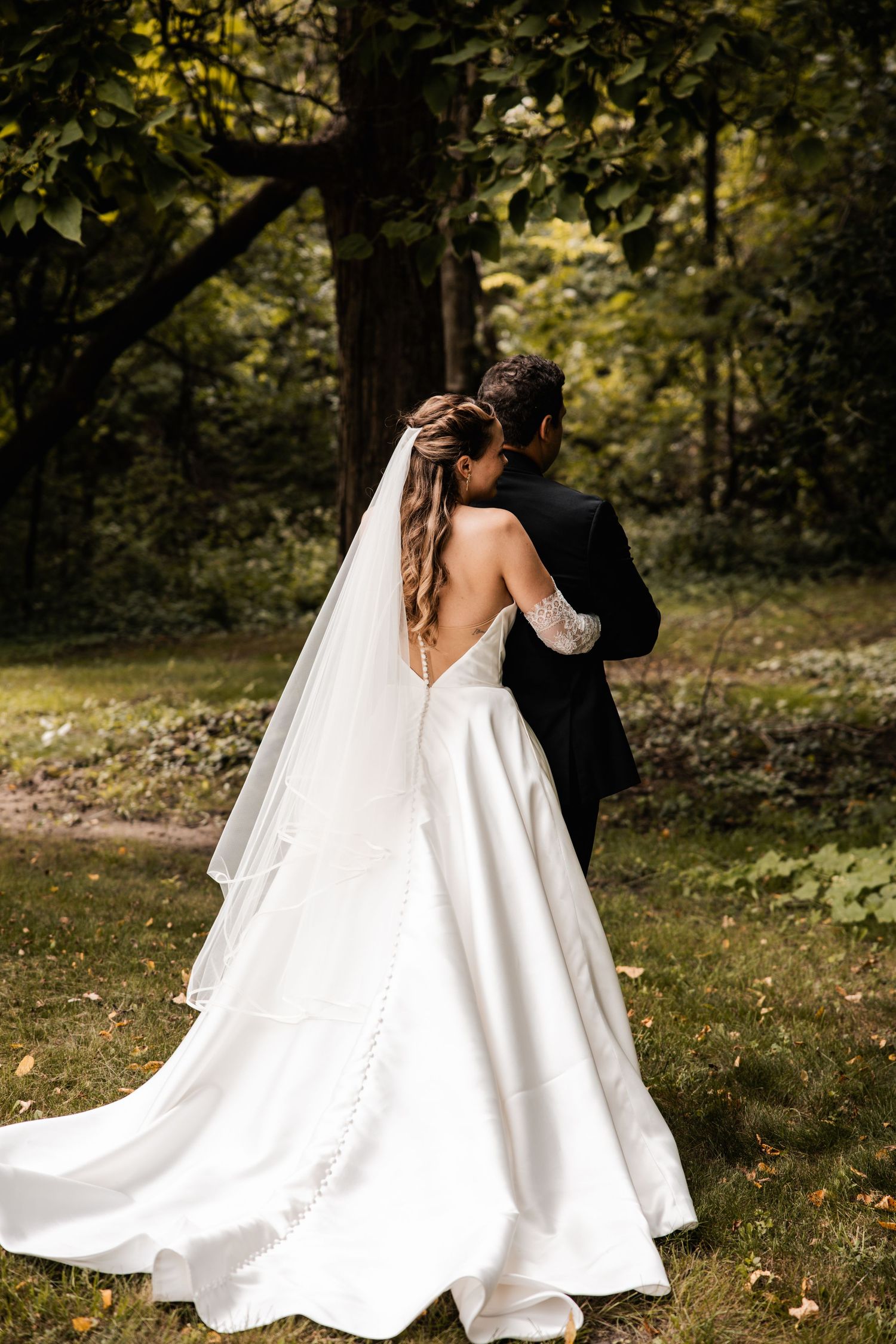 Romantic outdoor wedding photo of a couple embracing in a wooded setting.