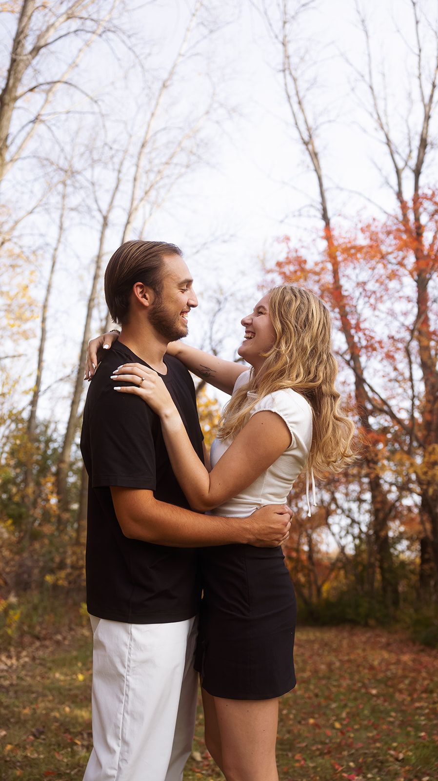 Couple in black and white clothing share loving moment in winter forest setting.