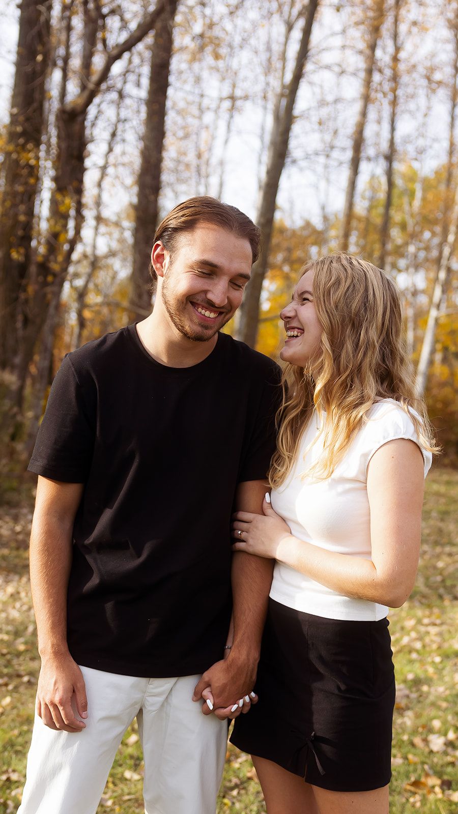 A couple shares candid moments of laughter in a fall forest setting.