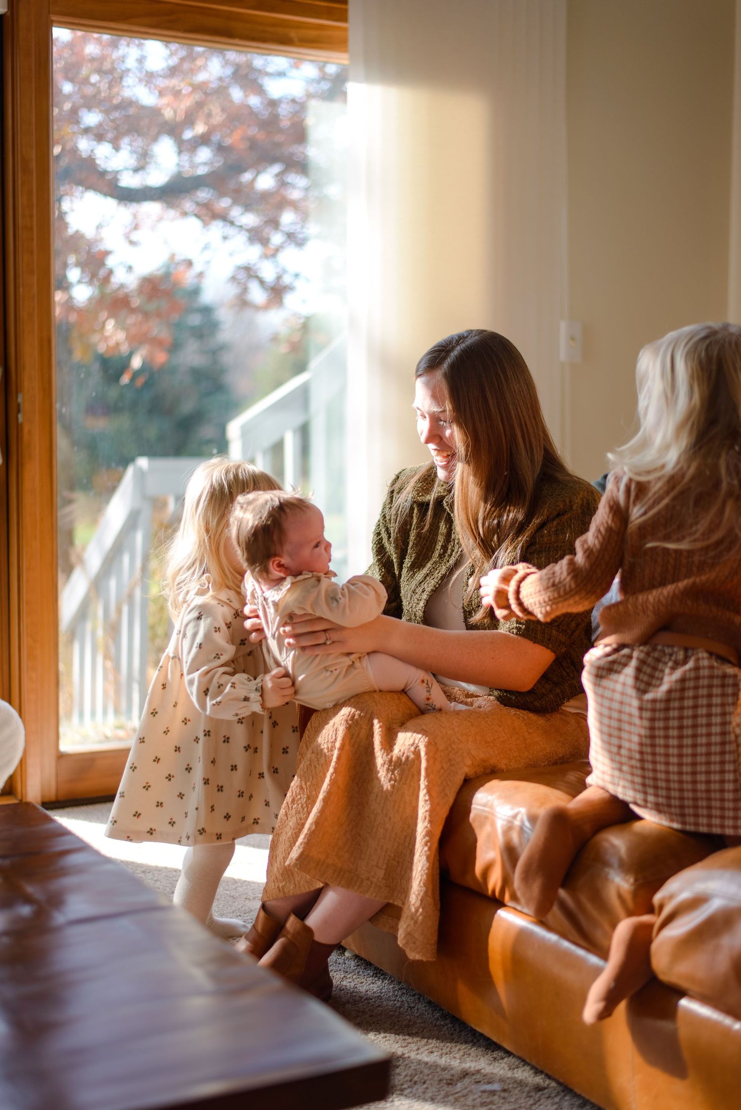 Mother cradling baby while daughter reaches in to kiss baby during in-home family session