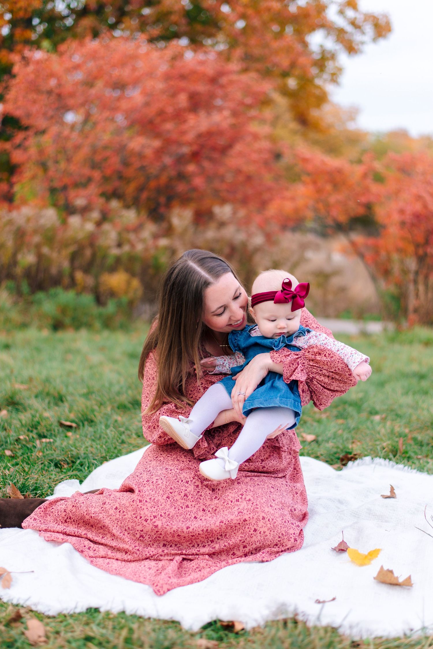 Mother cradles and kisses baby during outdoor fall maternity session