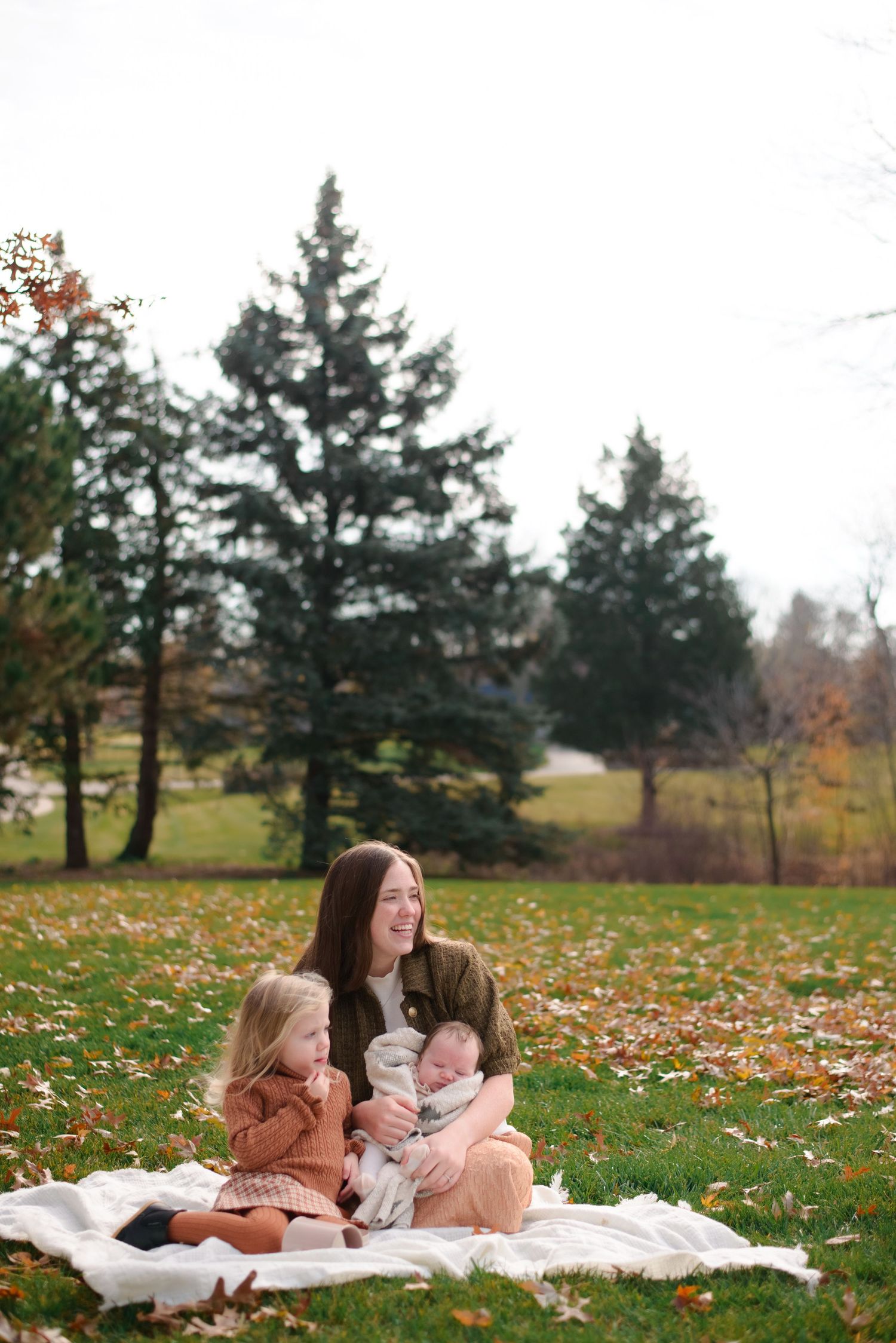 Mother embracing children on picnic blanket during fall outdoor photo shoot