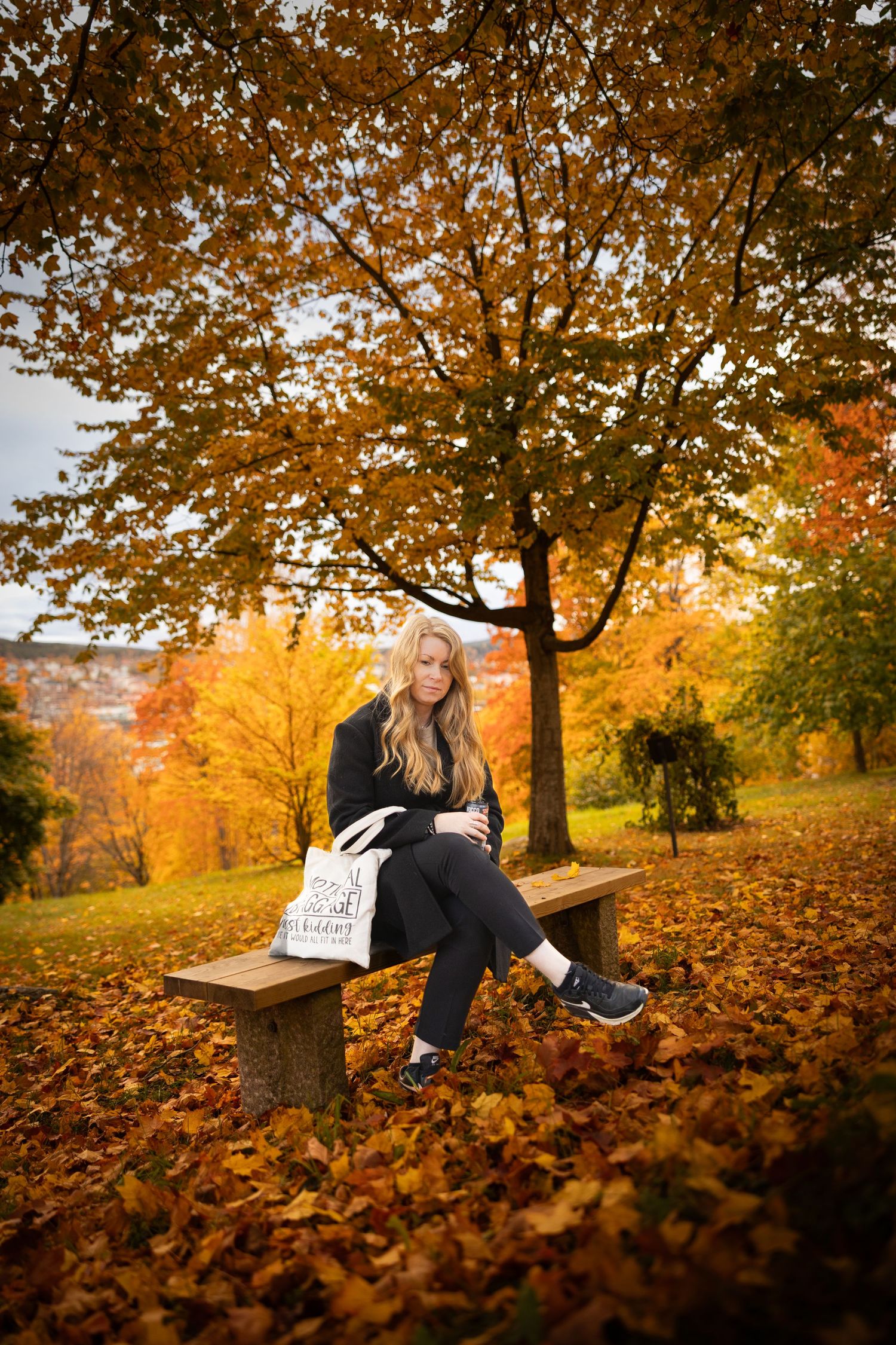 Person sitting among fallen autumn leaves under trees with golden foliage.