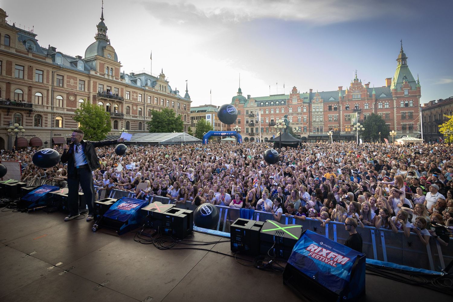Panoramic view of historic European city square filled with massive concert crowd.