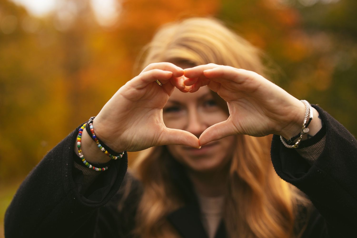 Hands making heart shapes against golden autumn foliage in soft focus.