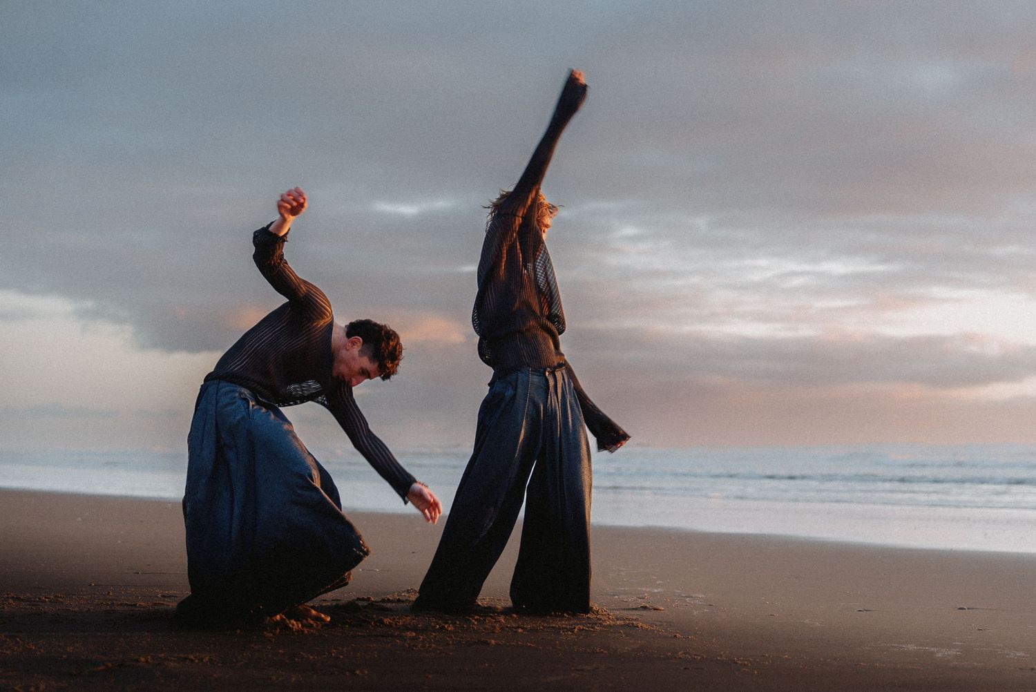 Duo en mouvement sur la plage au crépuscule, entre danse contemporaine et puissance expressive.