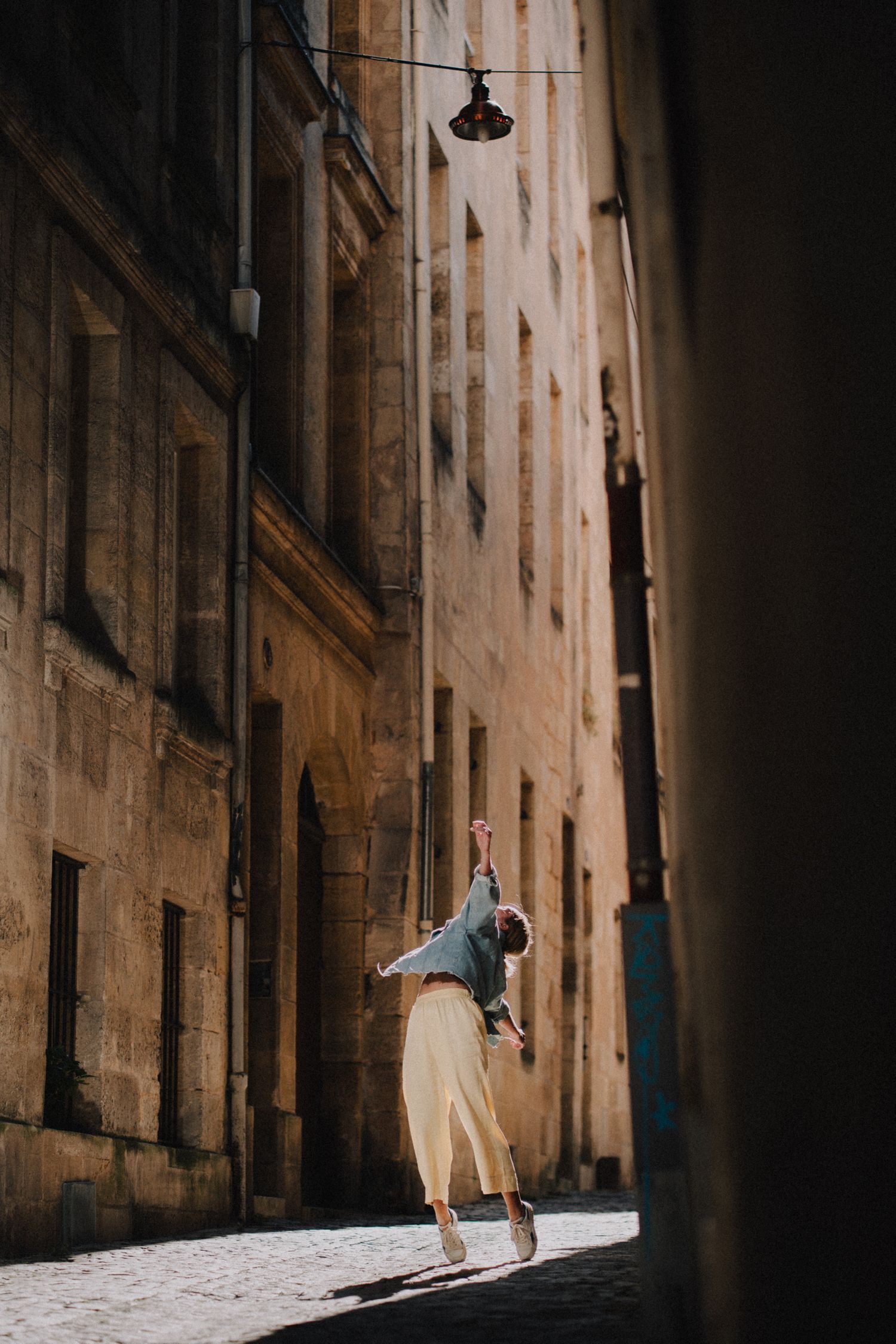 Danseuse effectuant un saut au cœur d’une ruelle ancienne, lumière naturelle, capture en mouvement.