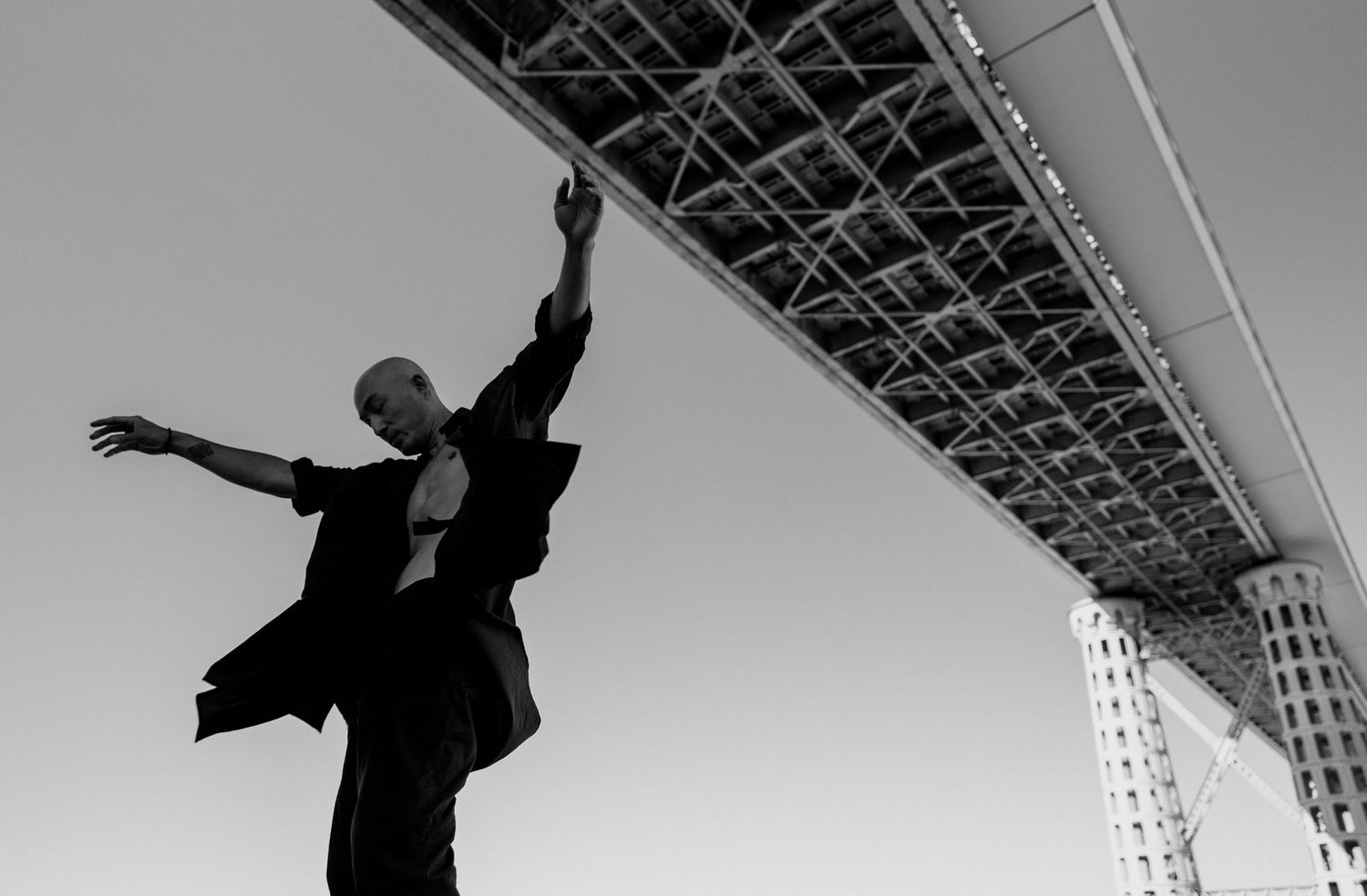 Danseur en plein saut sous un pont, en noir et blanc, capturant l’élan et l’architecture urbaine.