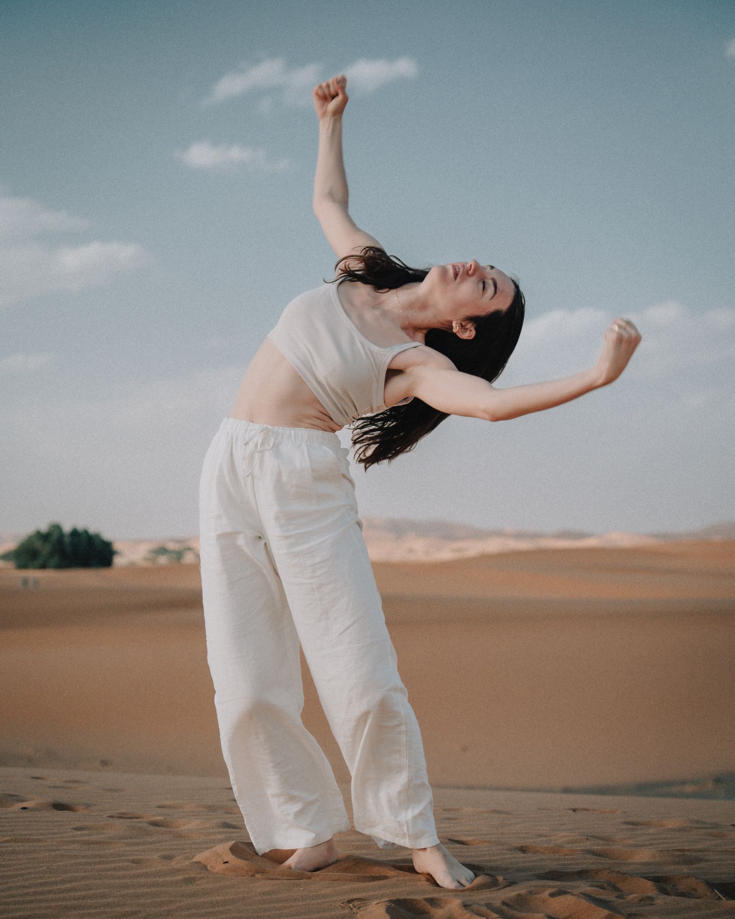 Danseuse en tenue blanche effectuant un mouvement fluide dans les dunes à Merzouga, Maroc.