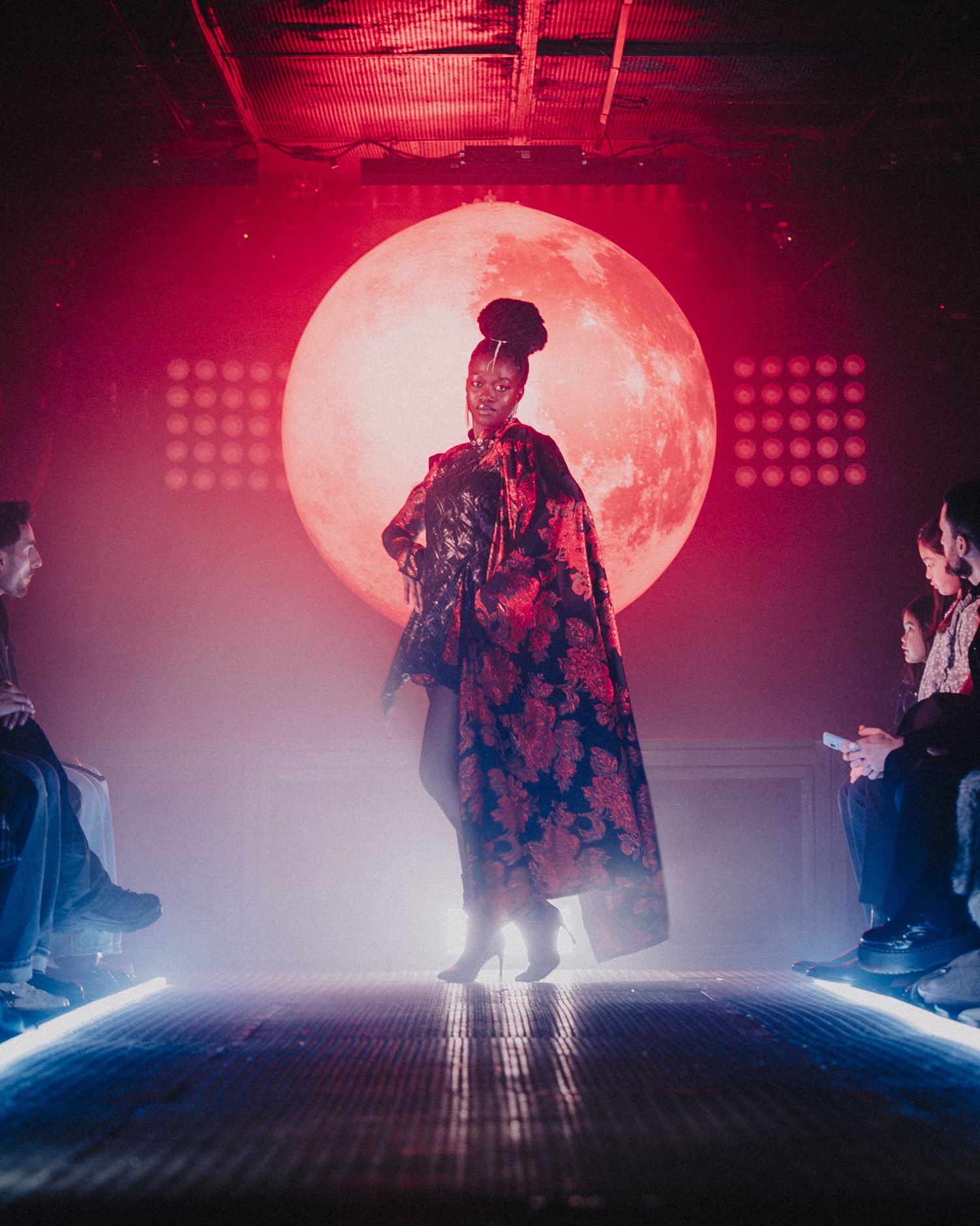 Silhouette d’un mannequin sur scène mode, lumière rouge dramatique, ambiance futuriste et stylisée.