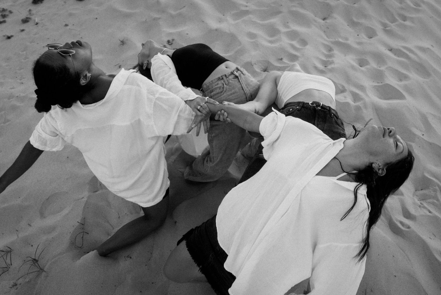 Photo chorégraphique en noir et blanc de danseuses allongées dans le sable, composition artistique.